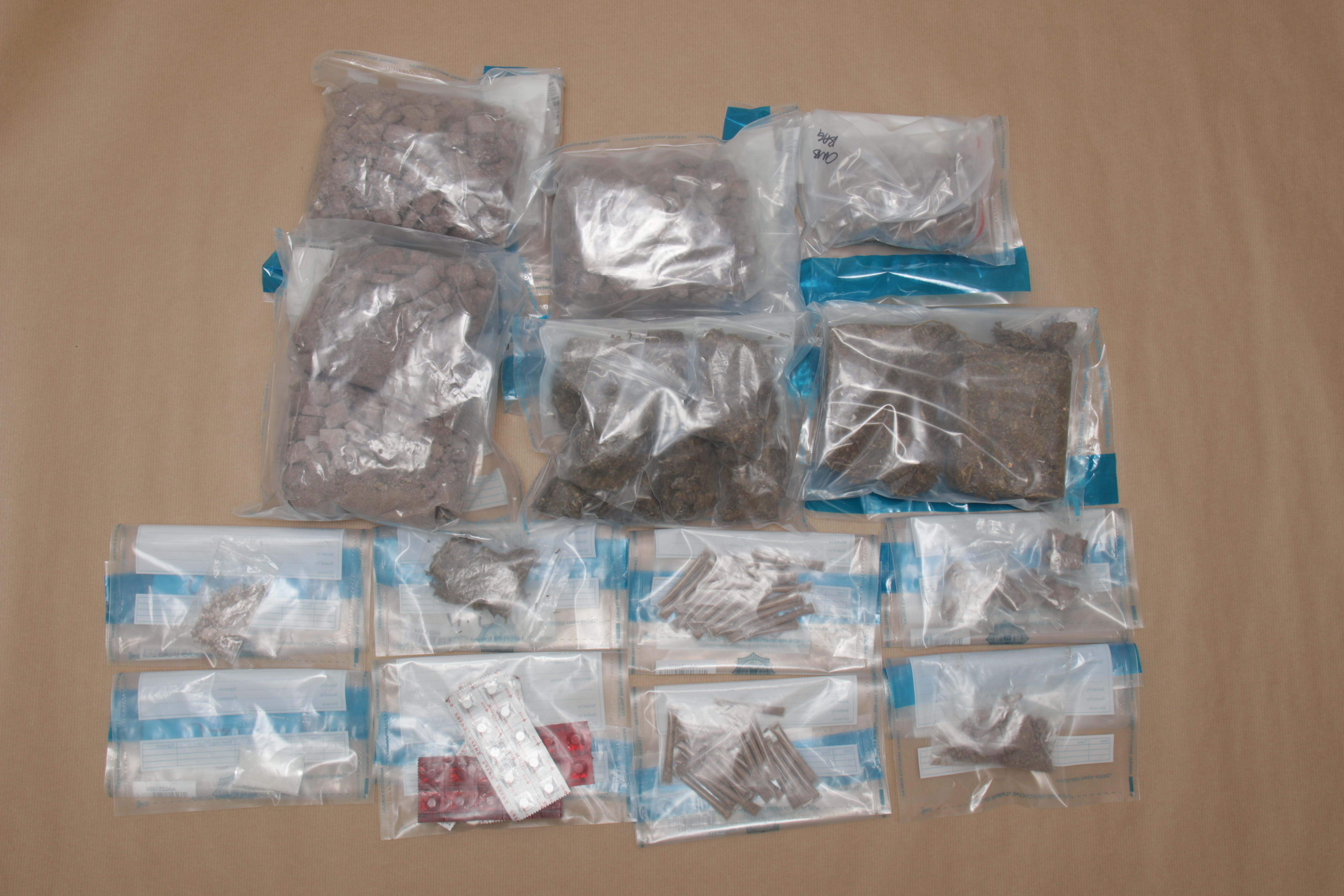 Plastic bags with pills, chunks, and plant matter organized on a brown surface.