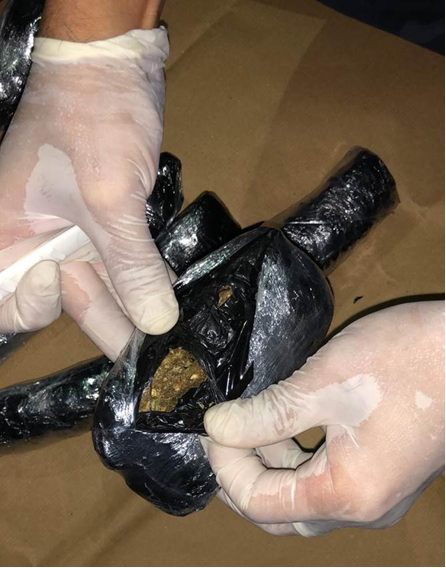 Gloved hands examine black-wrapped packages, one with a torn spot showing plant material.