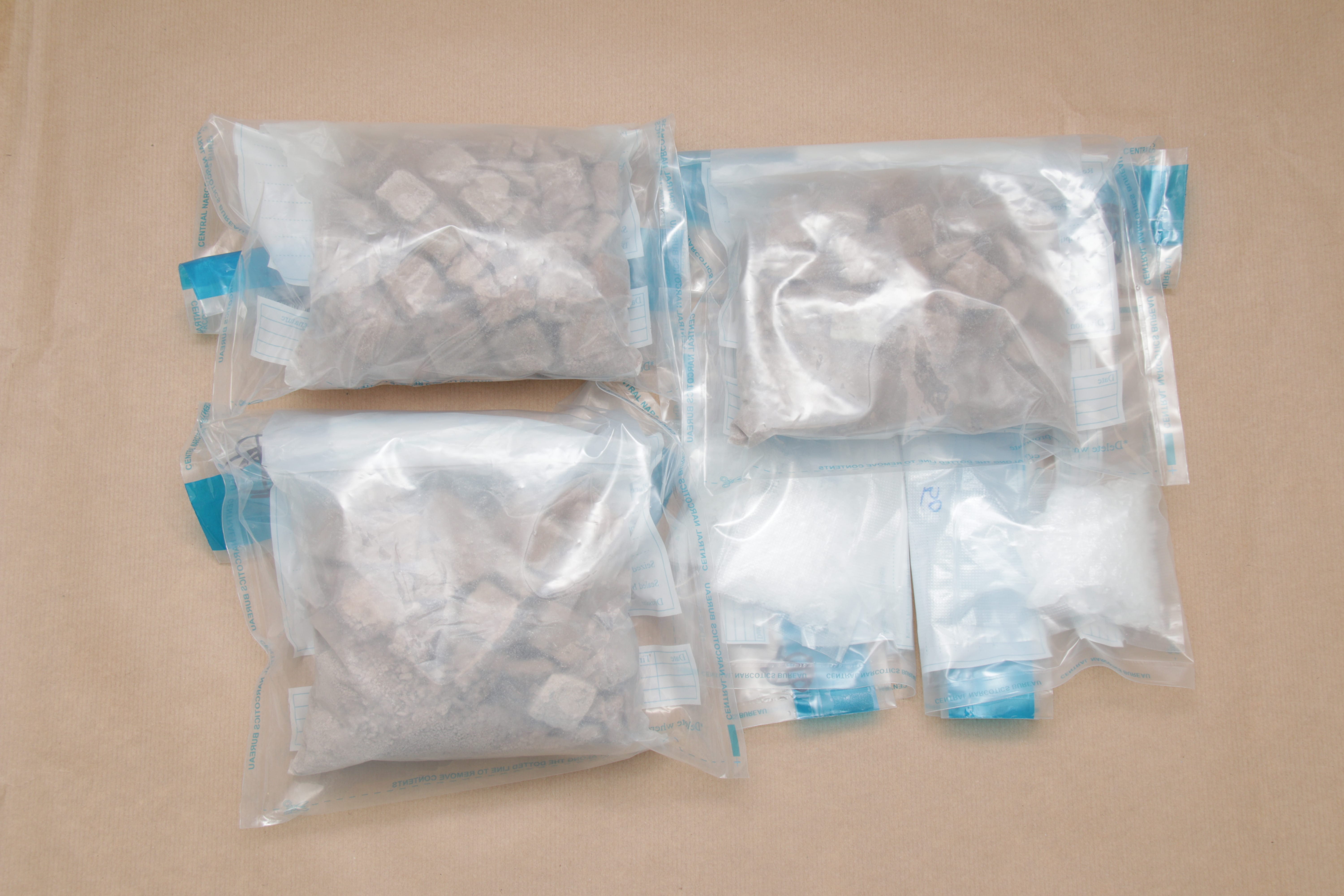 Sealed evidence bags with suspected drugs on brown surface.