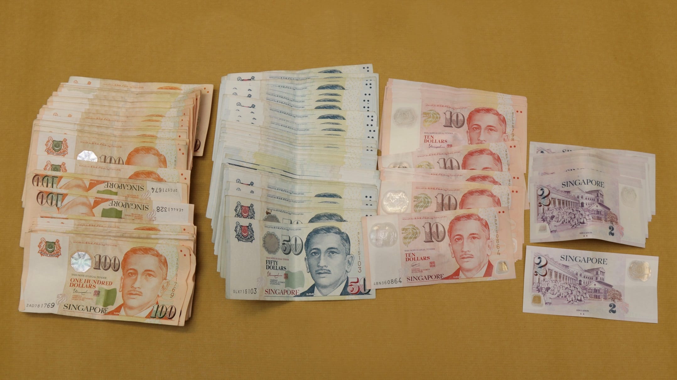 Stacks of Singapore dollar banknotes of various denominations on a gold surface.