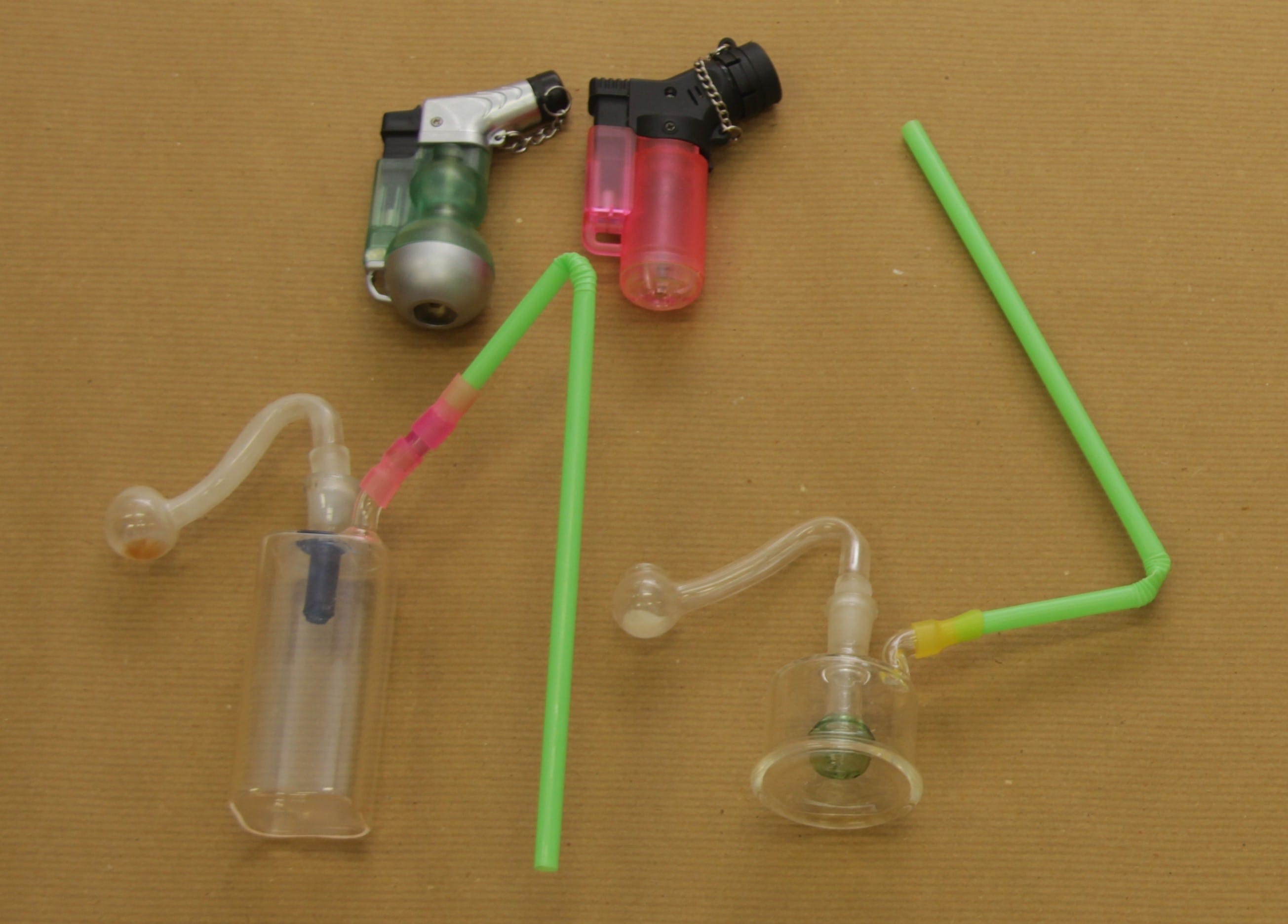 Two small glass pipes, two torch lighters, and green straws on a brown background.