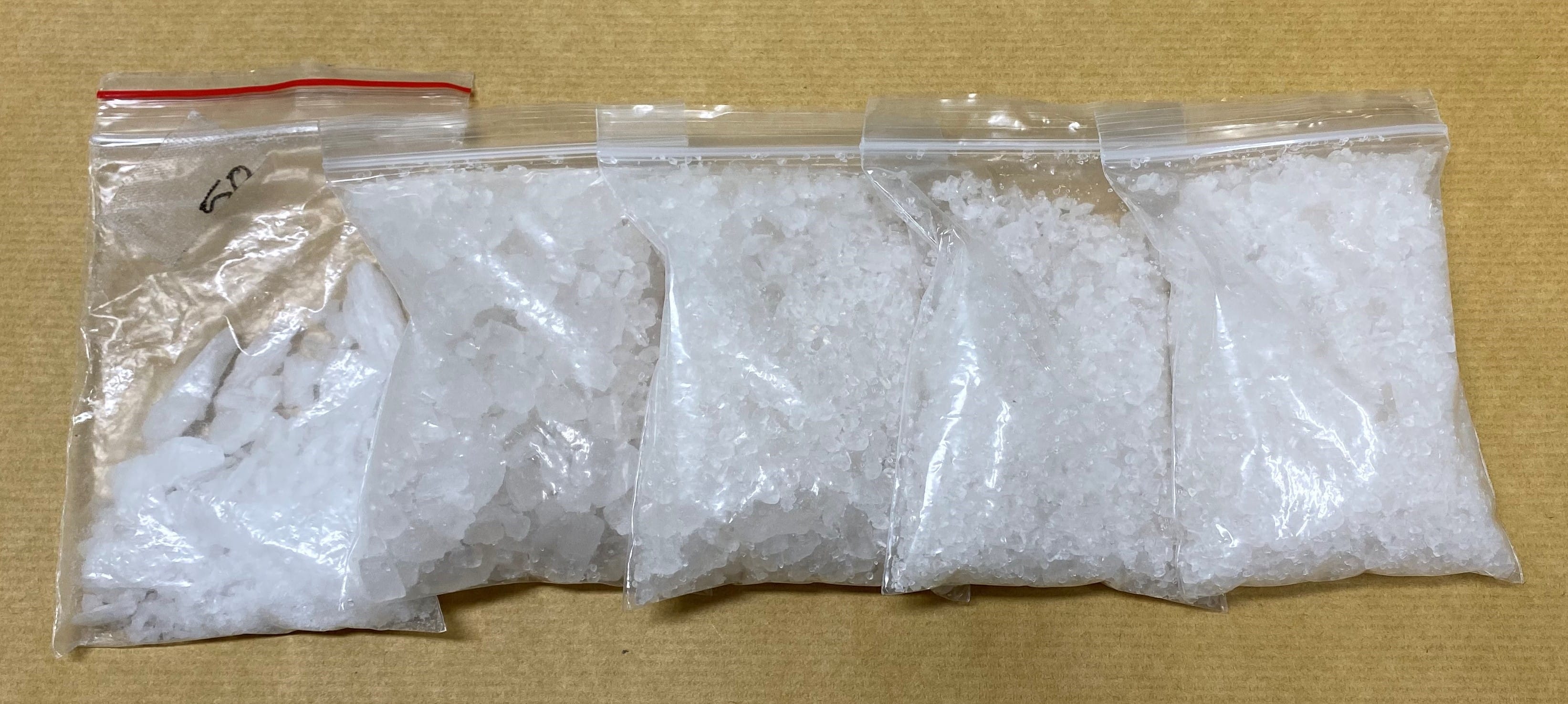 Five small ziplock bags filled with white crystalline material on a brown surface.