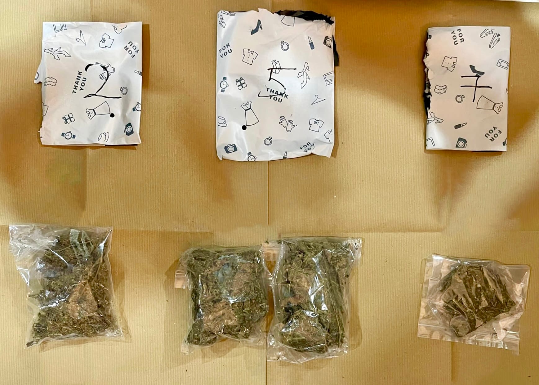 Three white gift bags with 'thank you' prints above four small bags of green dried herbs.