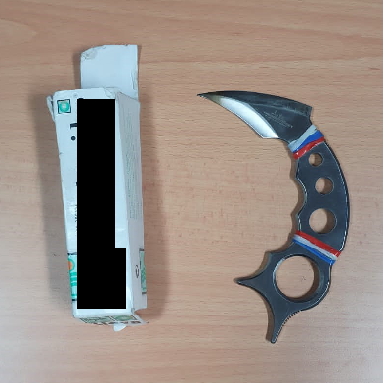 Karambit knife with black handle, red/blue stripes, and box on a wood surface.