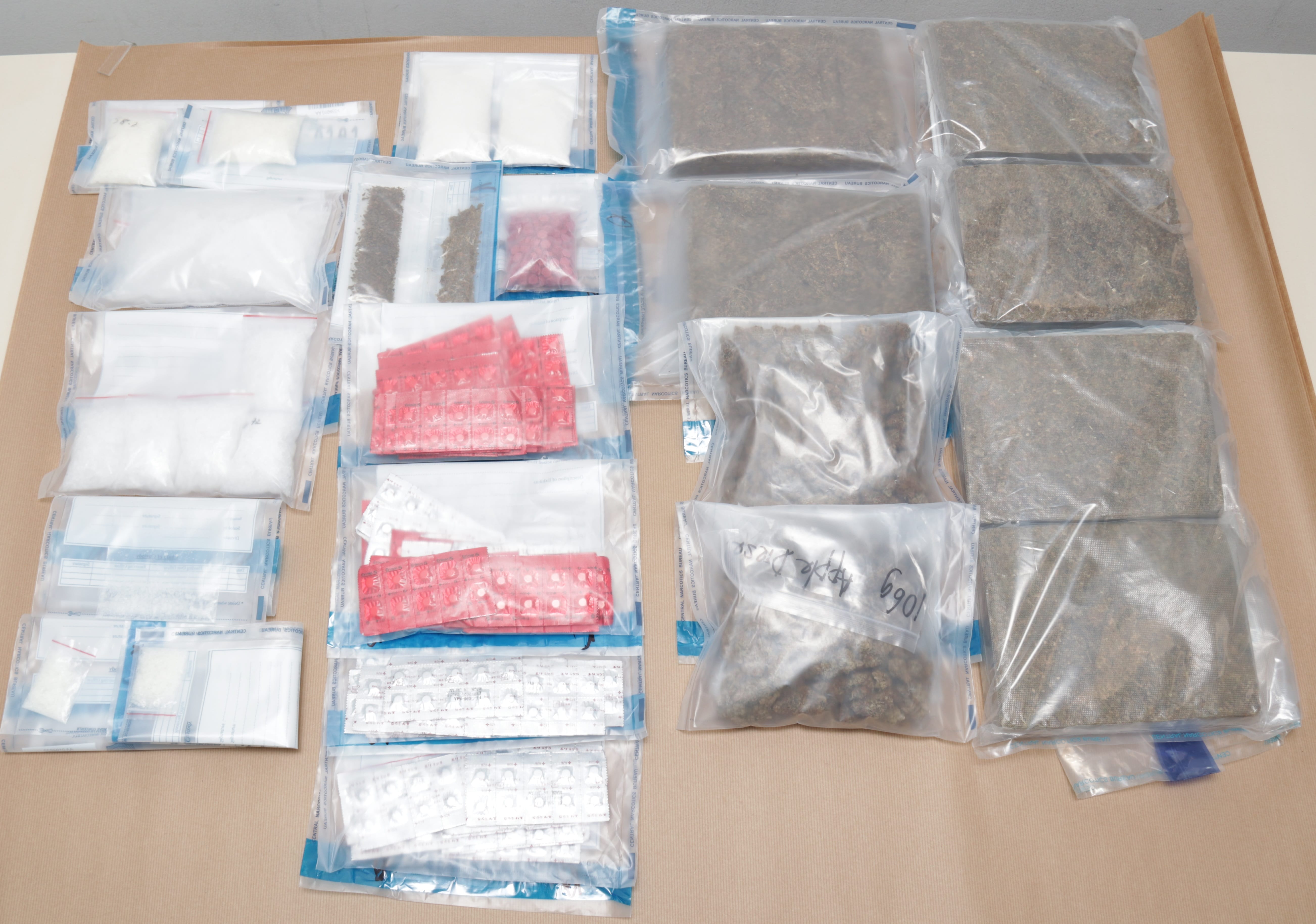 Seized items: bags of white powder, cannabis bricks, pills in blister packs on a brown surface.