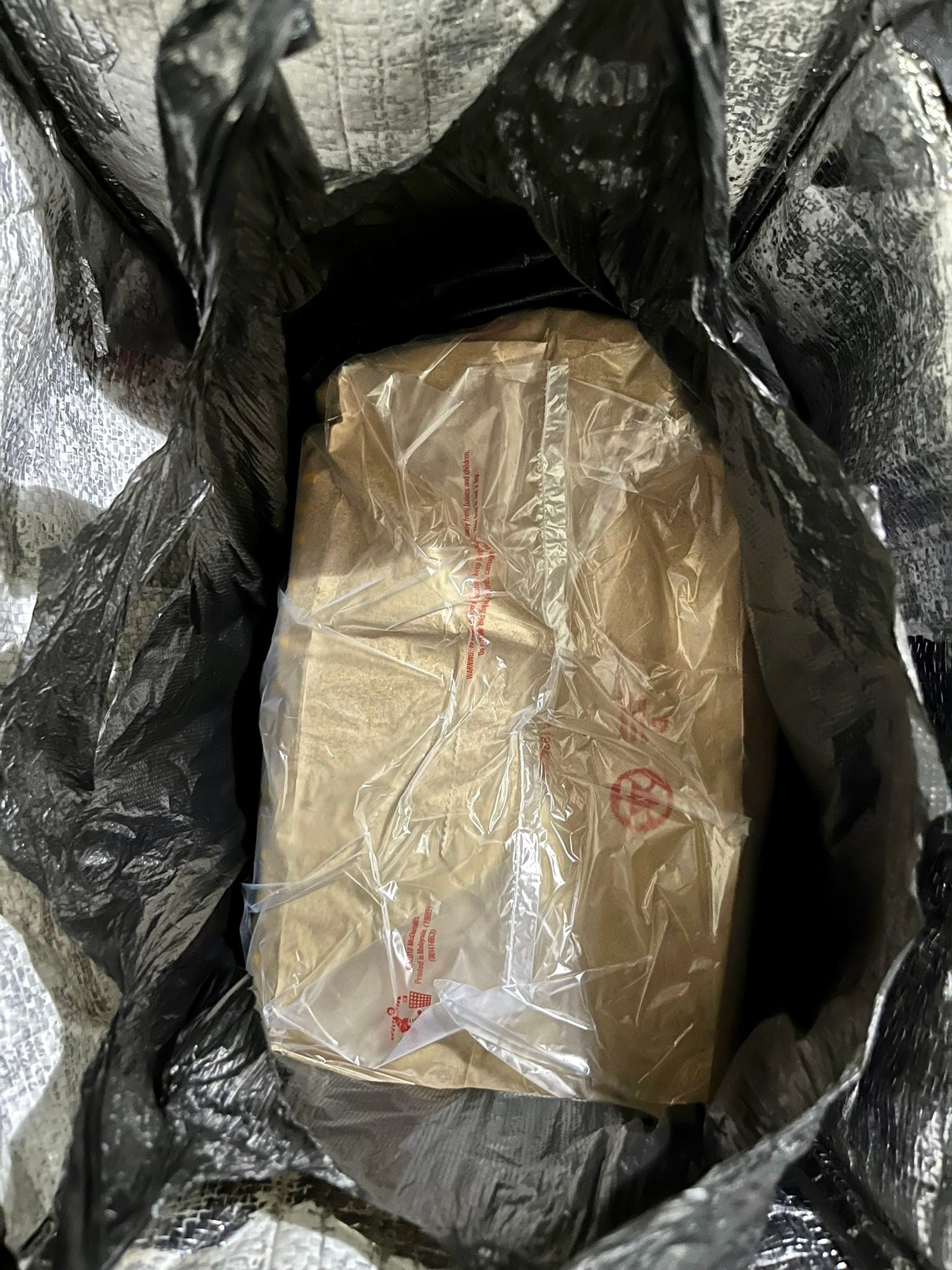 Brown paper bag wrapped in clear plastic inside a black and silver insulated bag.