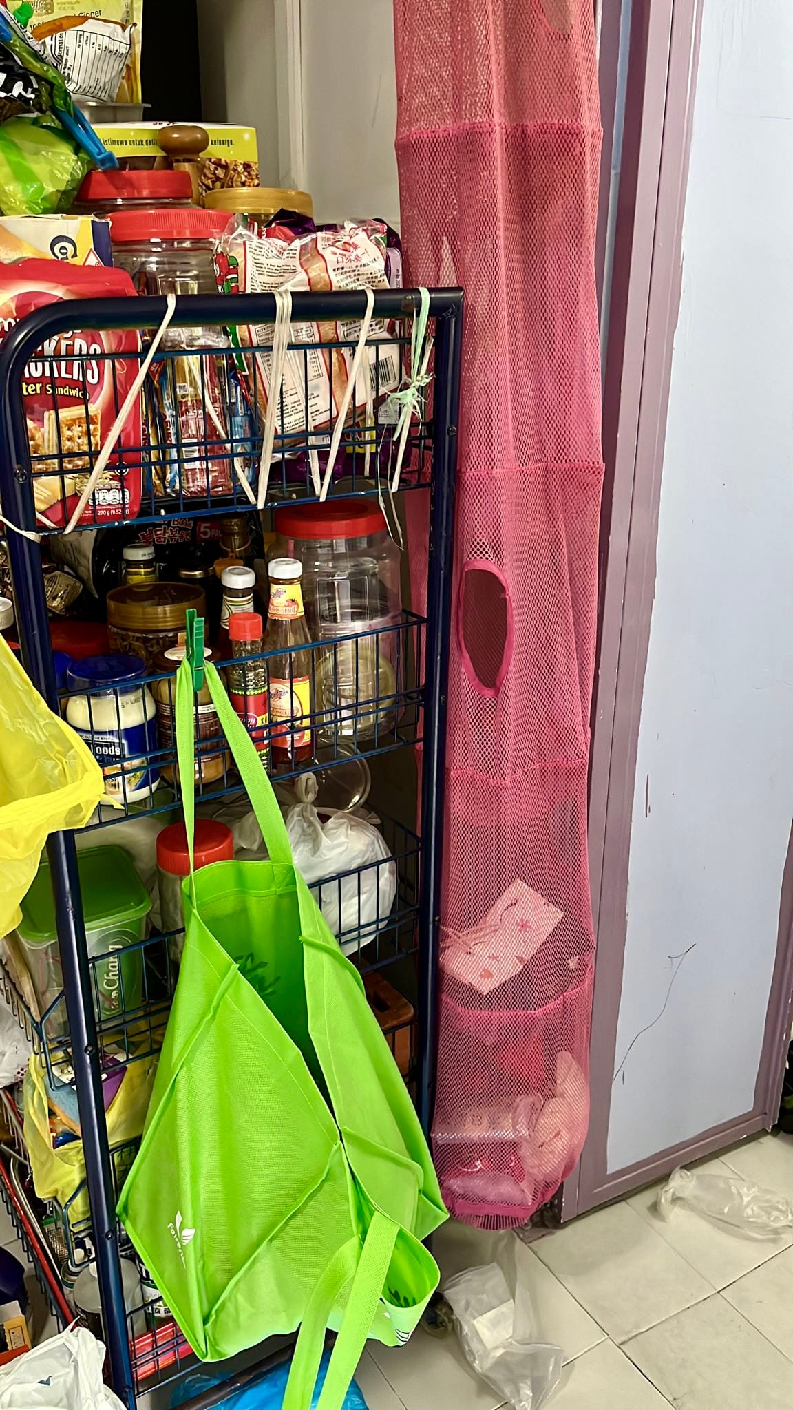 Shelves with food items, green shopping bag, and pink mesh hanging storage.