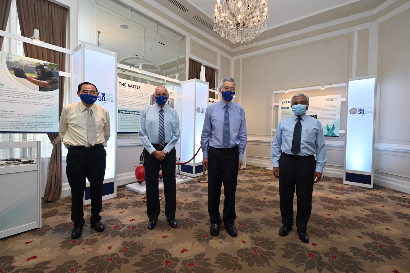 Four men in dress shirts and face masks stand in front of CNB 50th anniversary displays.