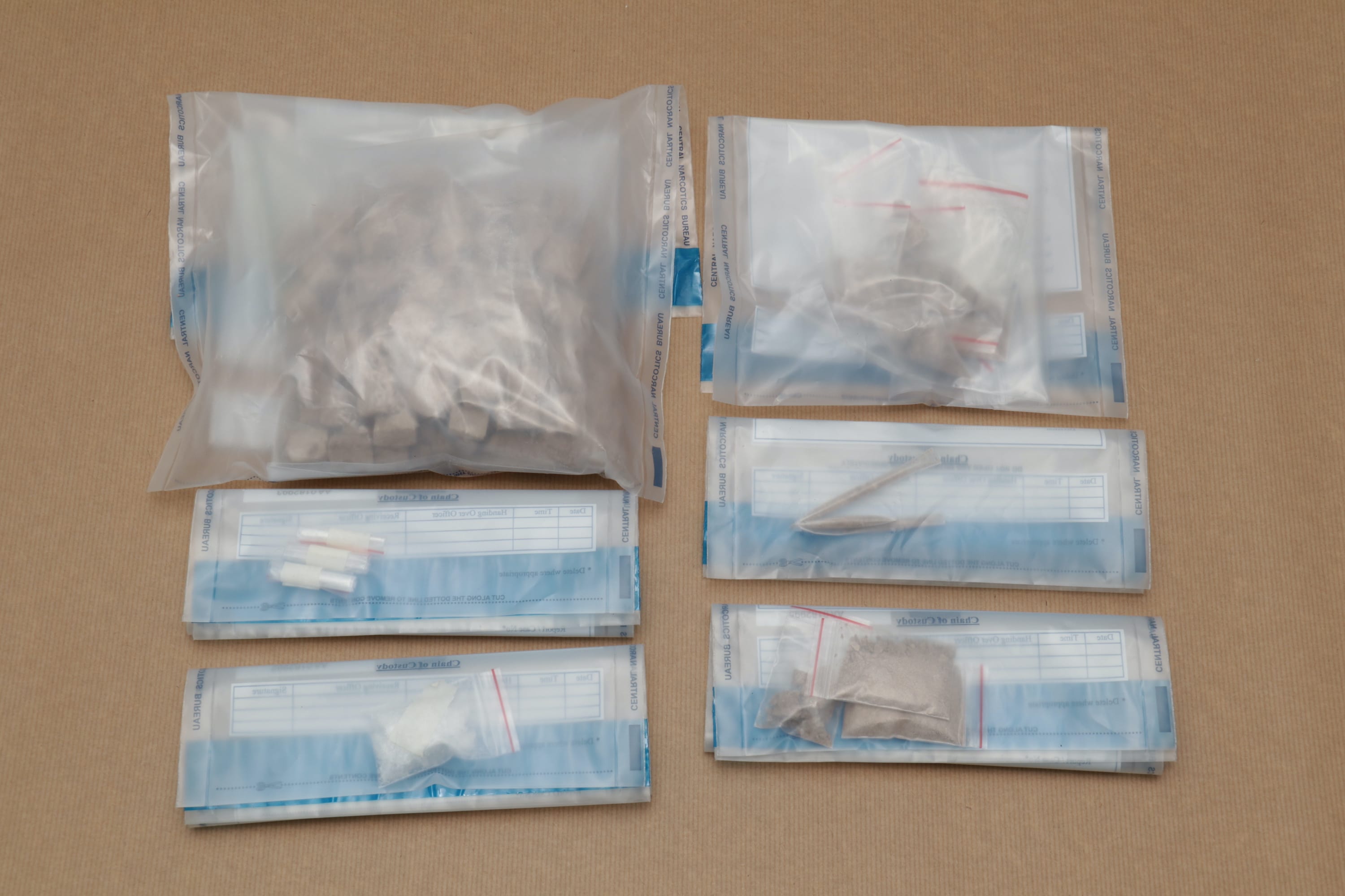 Evidence bags of substances, including chunks, powder, and capsules, on a brown surface.