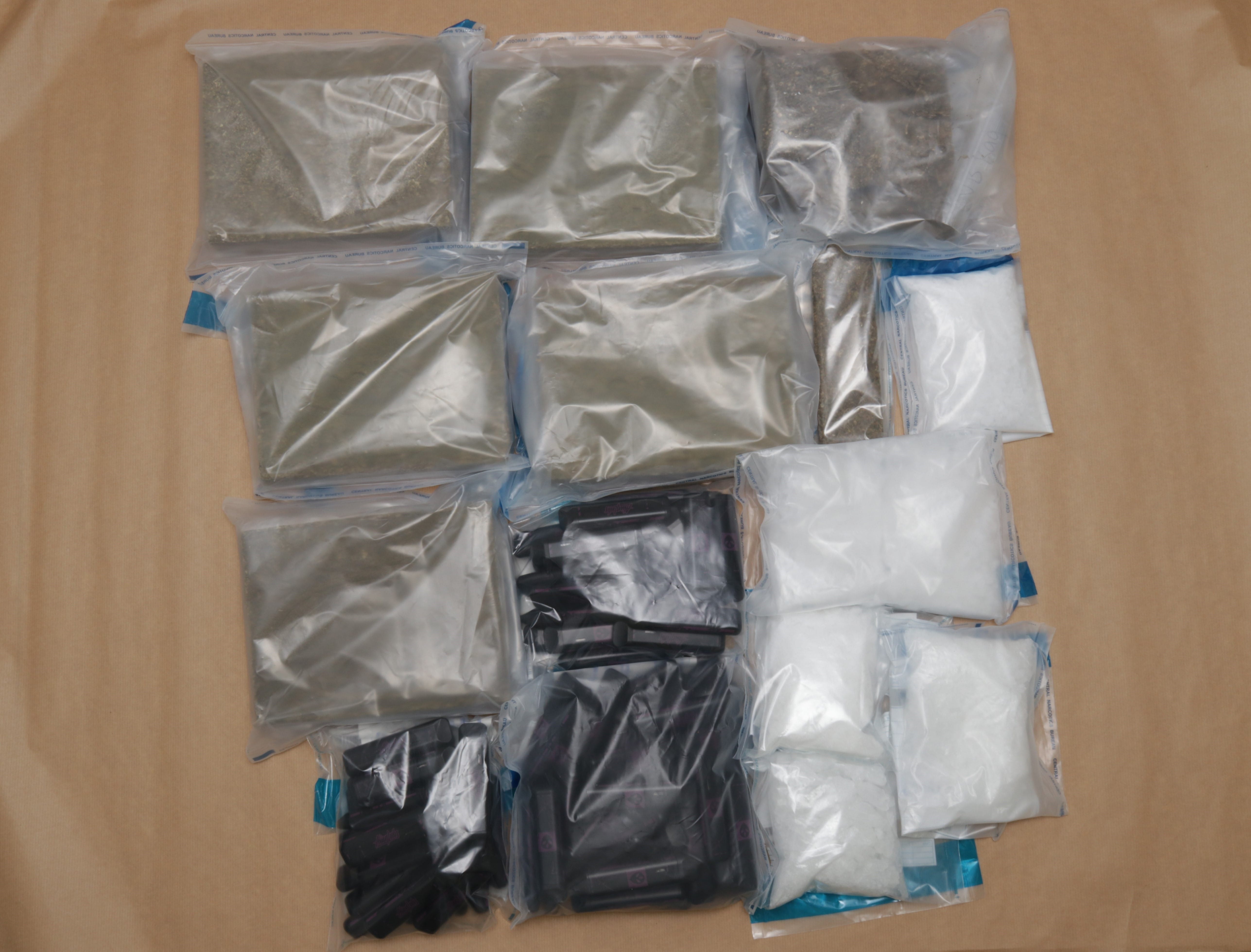 Various plastic bags containing plant matter, white powder, and cartridges on brown paper.