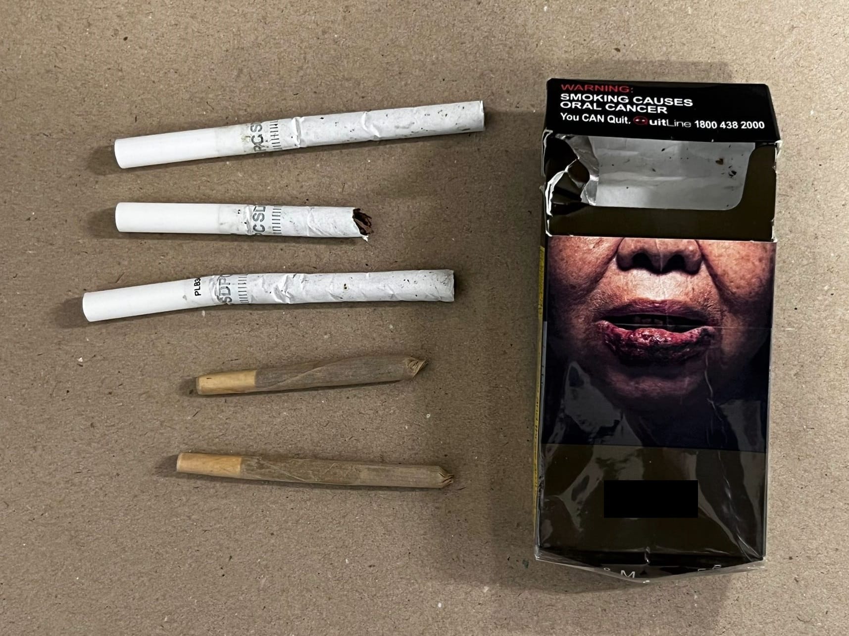 Open cigarette pack with graphic warning and loose cigarettes and hand-rolled joints.