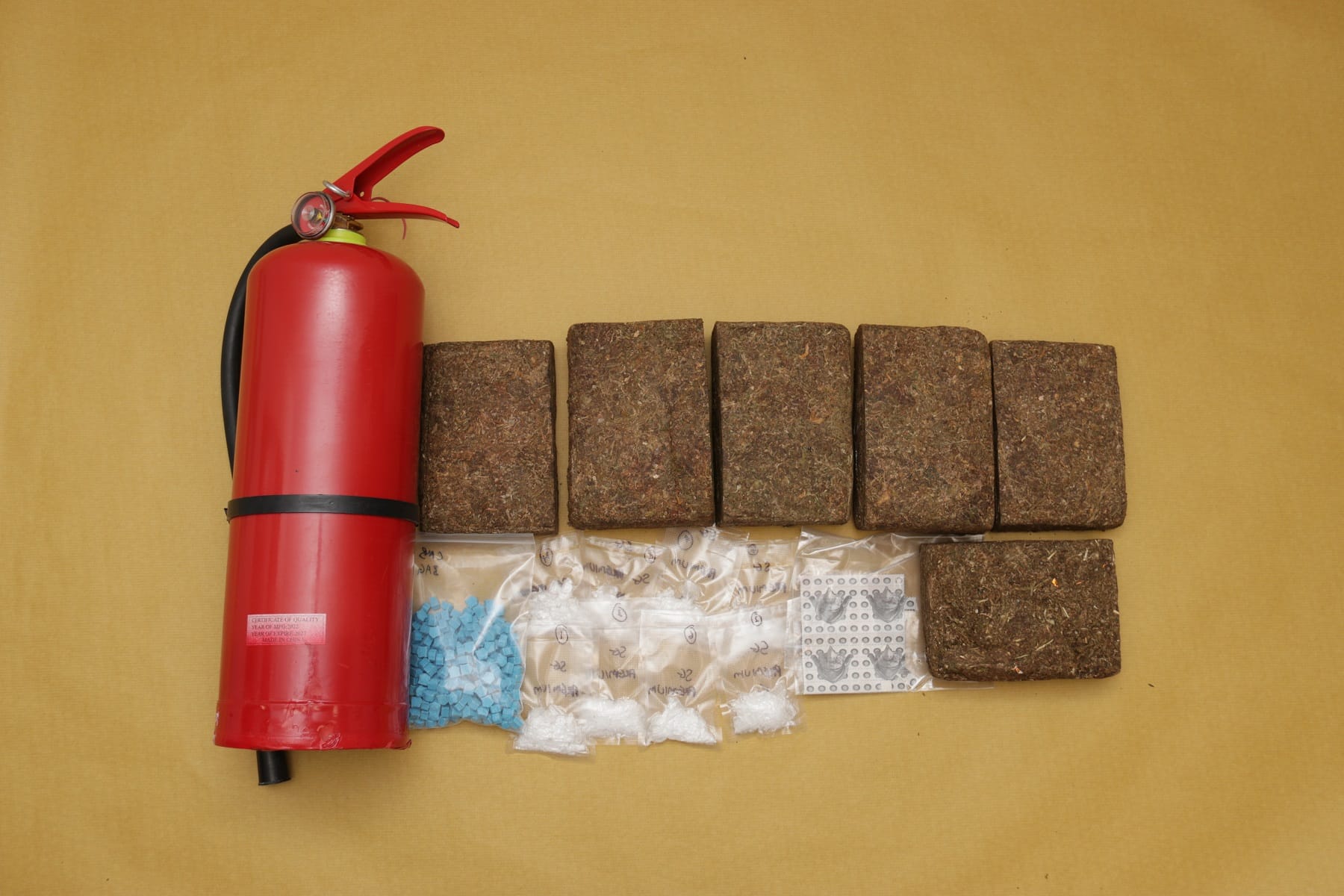 Red fire extinguisher, bricks of plant matter, and small bags with pills and white powder.