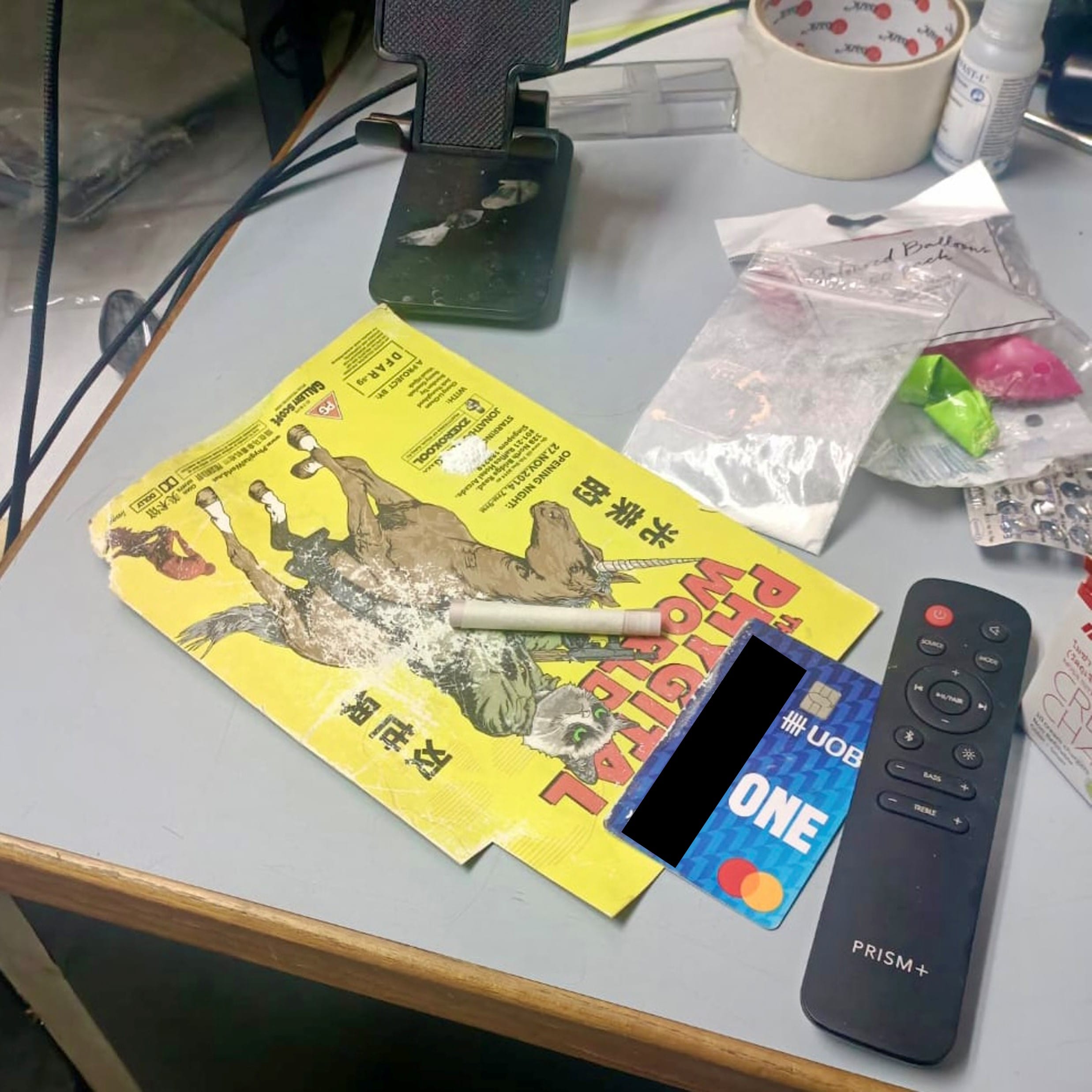 Desk with yellow flyer, UOB card, Prism+ remote, roll, balloon pack, tape roll, and other items.
