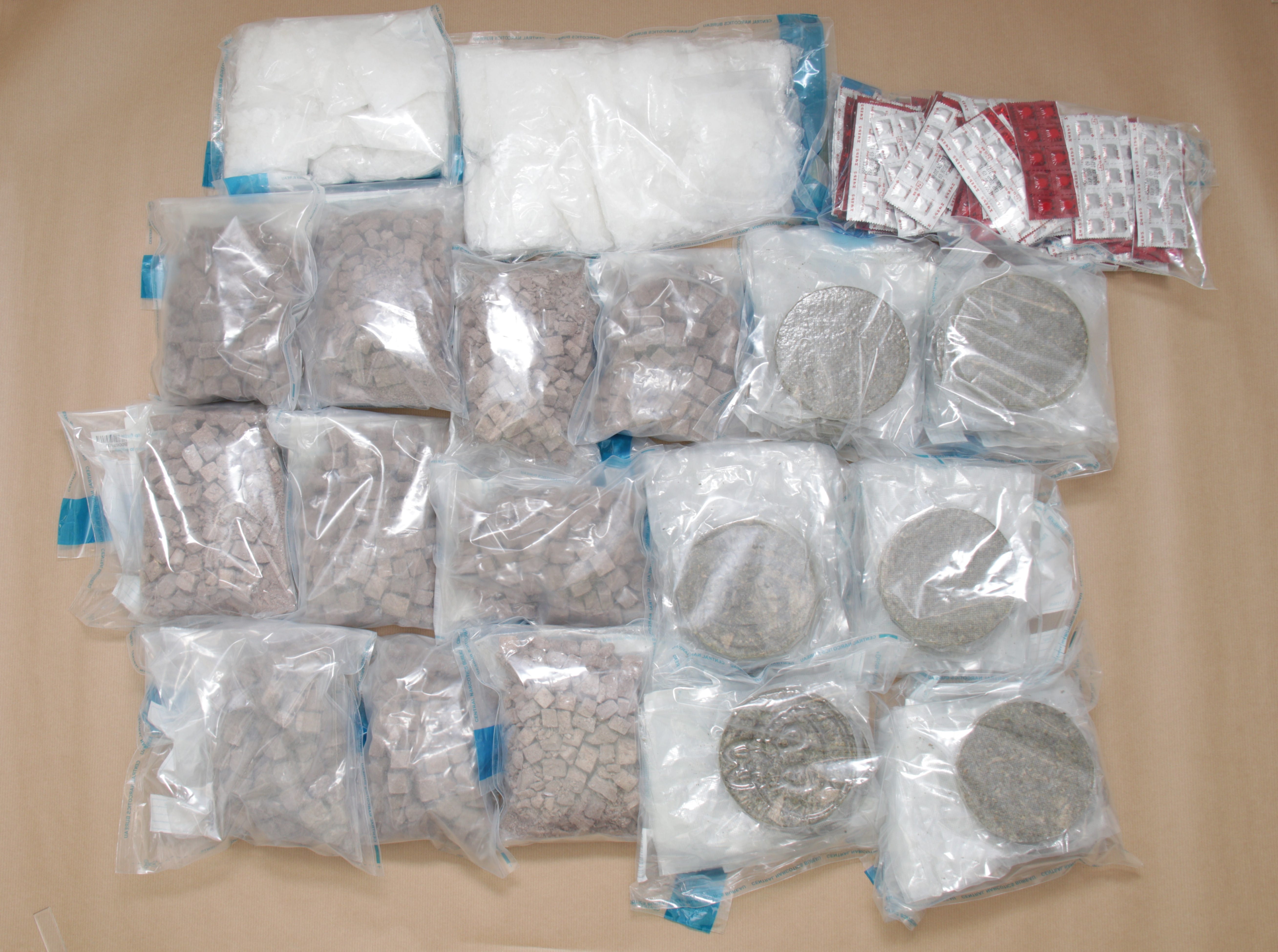 Clear plastic bags filled with white powder, brown cubes, and brown discs. Red and silver blister packs.
