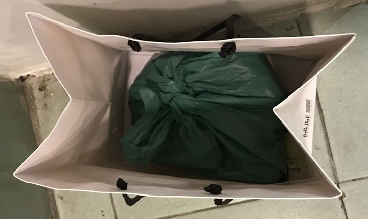 Open white shopping bag with black handles. A green plastic bag sits inside.