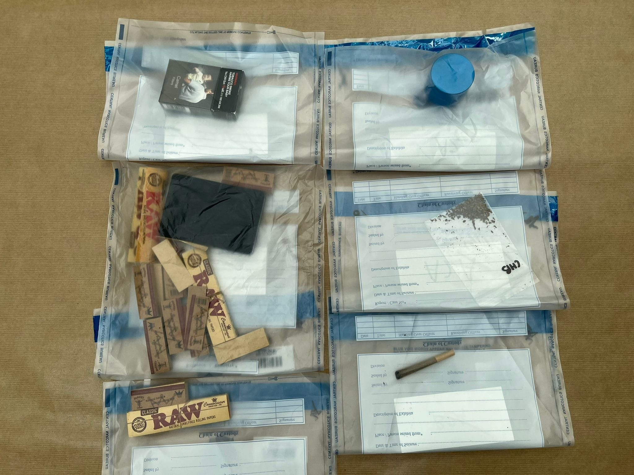 Evidence bags containing rolling papers, tobacco, a container, and a hand-rolled cigarette are on a table.