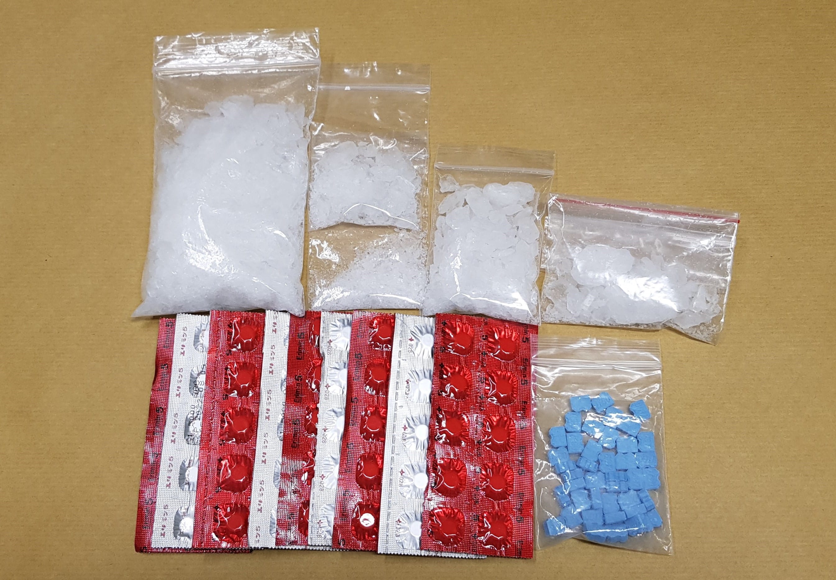 Bags of white crystals, blue pills, and red/silver foil-backed pills.