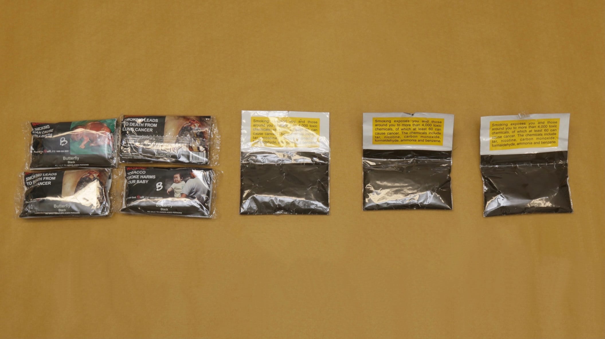 Packets of "Butterfly" black tobacco with health warnings and sealed bags of tobacco on yellow fabric.