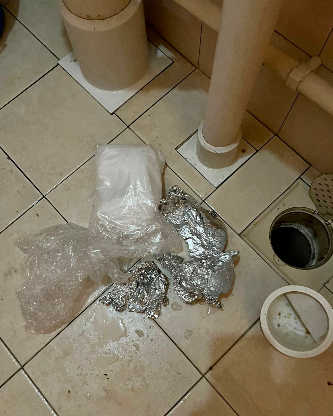 Tiled floor showing bags, foil, standing pipe, and open drain with removed cover.