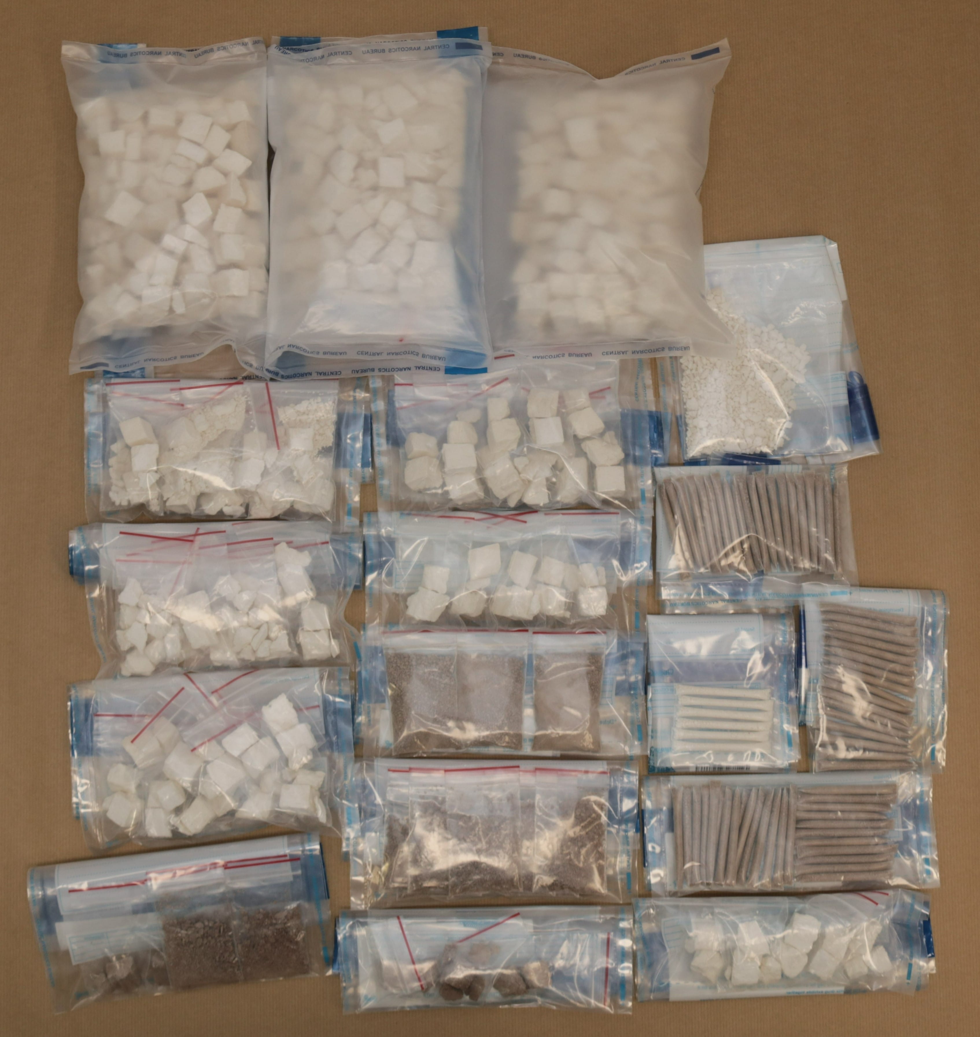 Sealed plastic bags containing various substances (white cubes, powders, rolled items) on a brown surface.