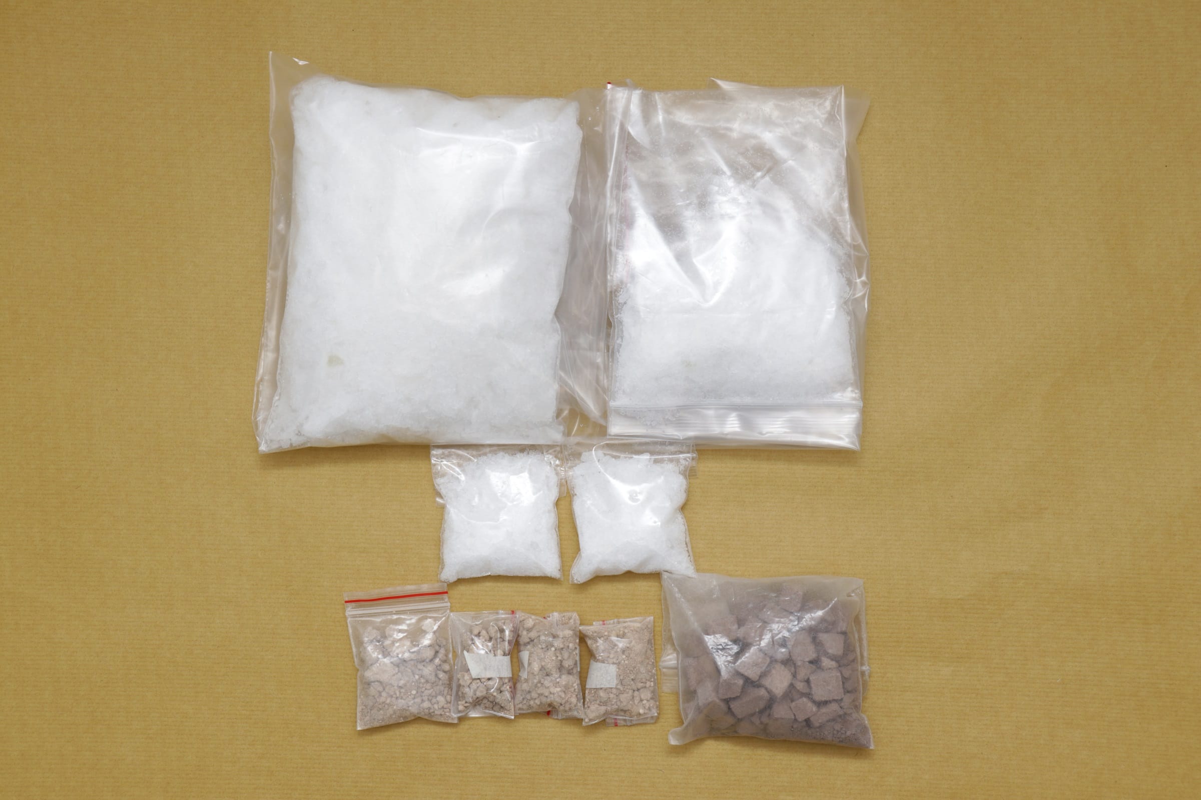 Several clear plastic bags containing substances, white and brown, arranged on a beige surface.