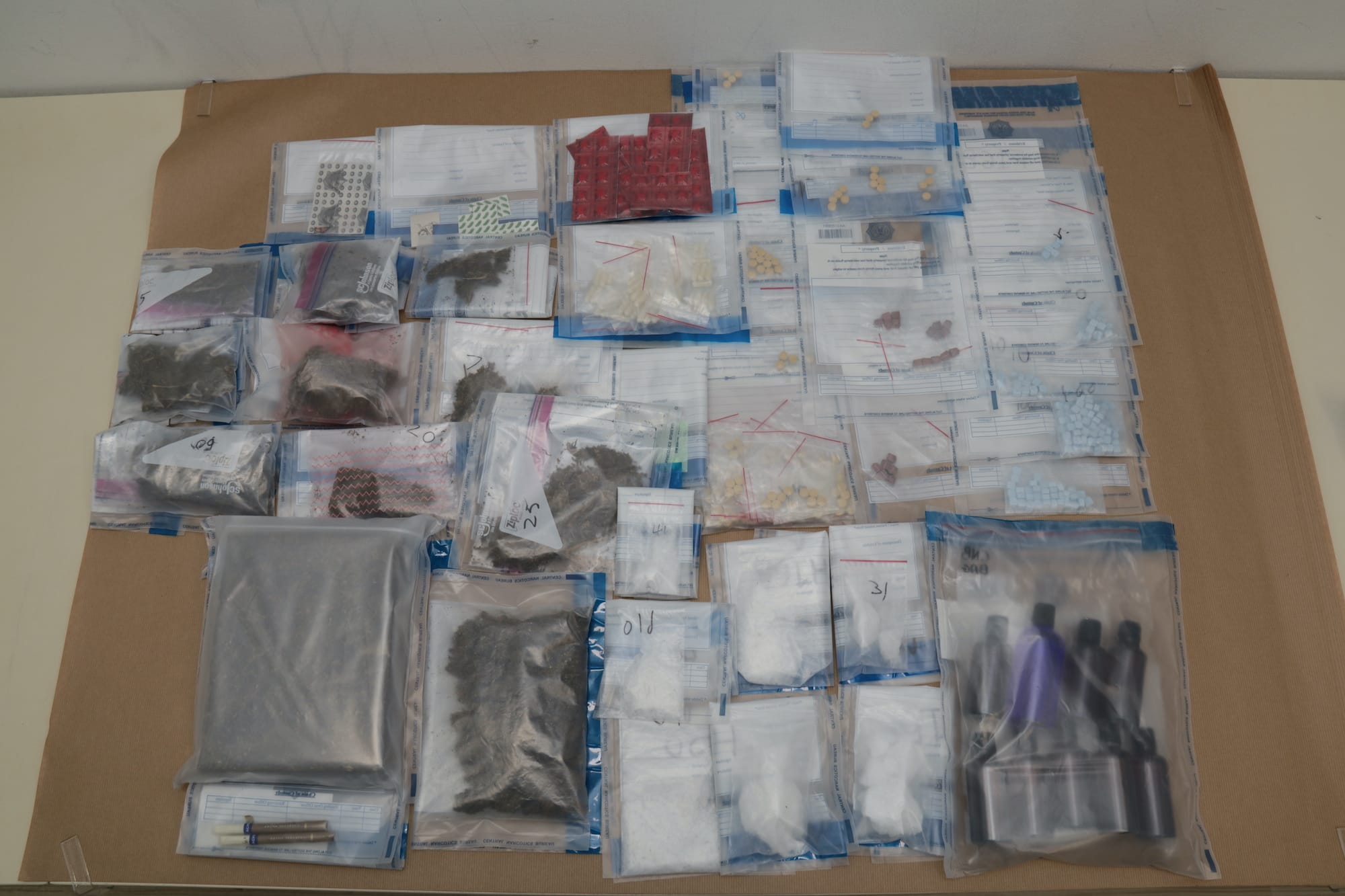 Various bagged substances and pills on evidence table.