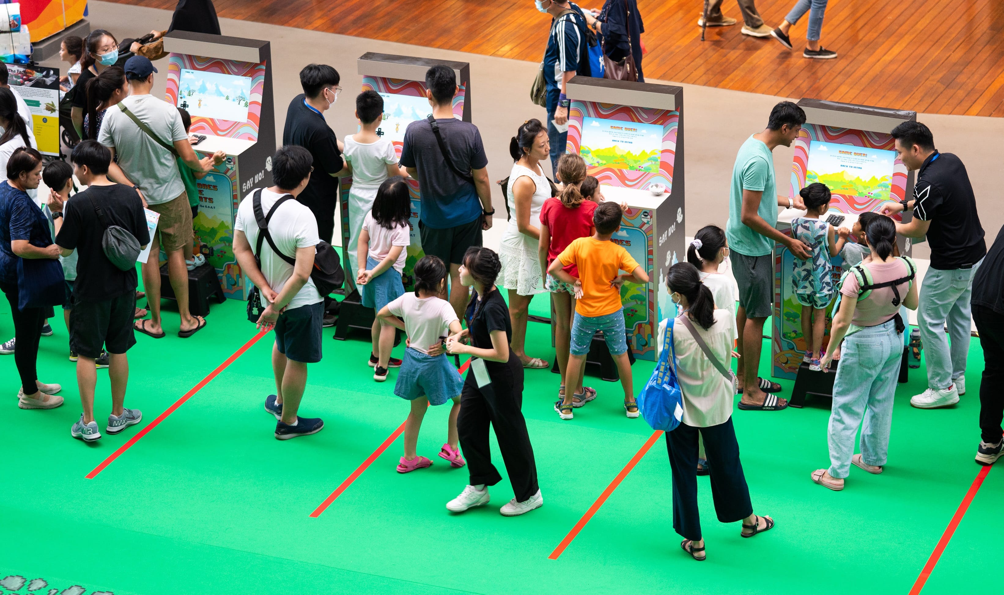 People around retro arcade games on green carpet with red lines.