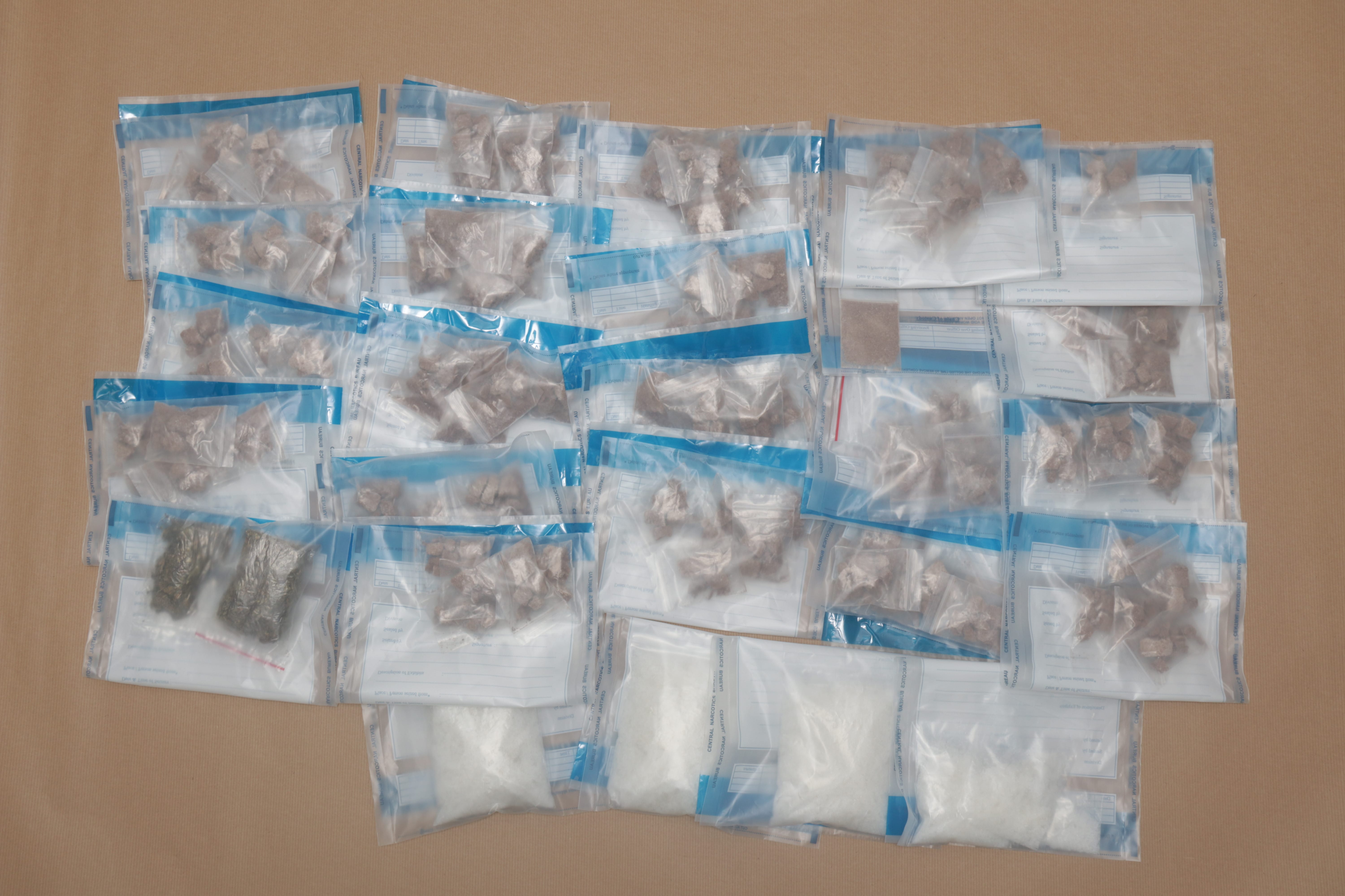 Multiple bags of brown and white substances sealed in "Central Narcotics Bureau" bags on a tan surface.