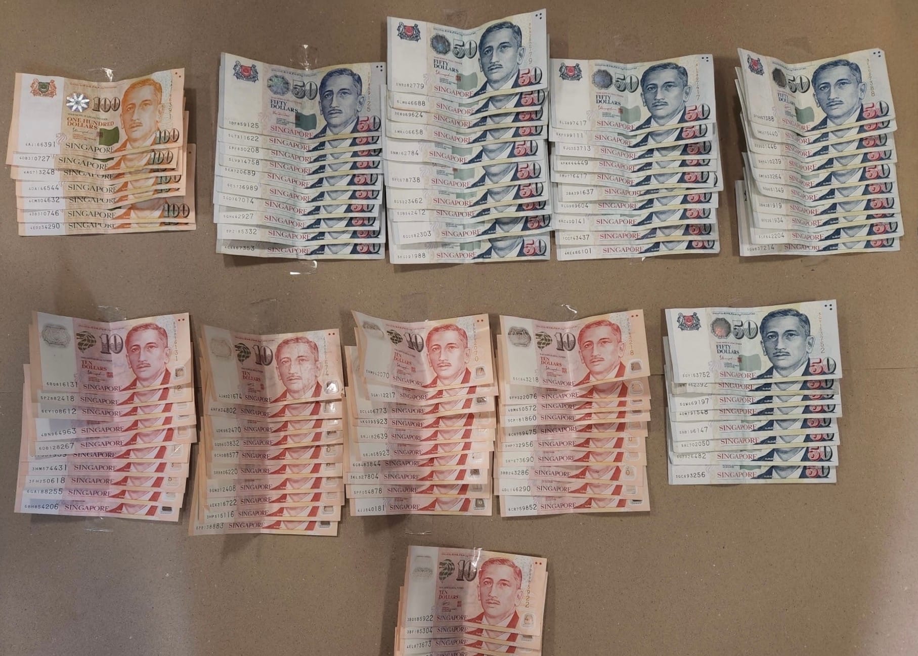Stacks of Singapore dollar banknotes: Hundreds, Fifties, and Tens, arranged on a flat surface.