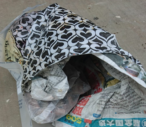 Overstuffed bag with black heart pattern, filled with crumpled newspapers and plastic bags.