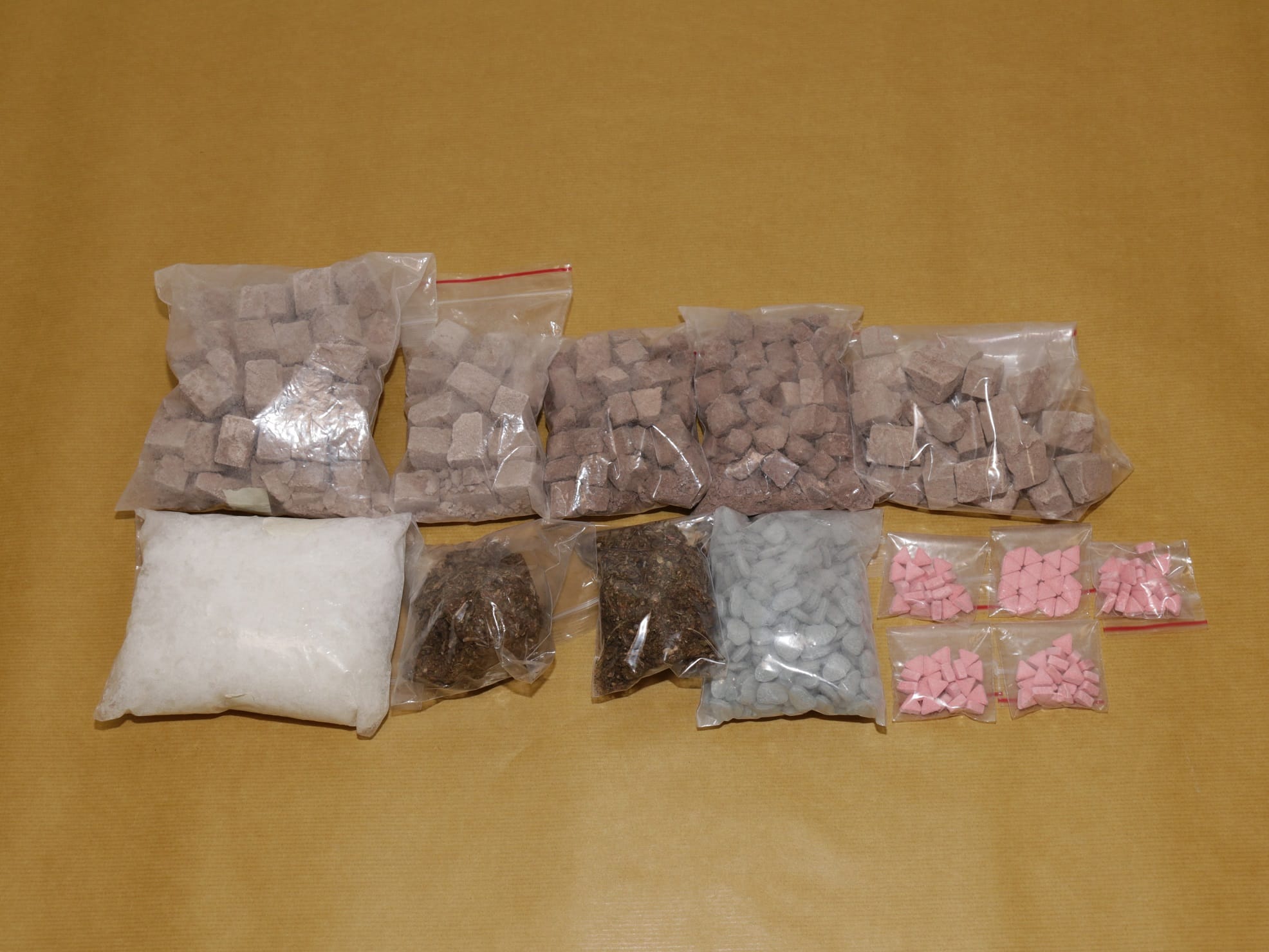 Clear plastic bags filled with various colored materials, cubes, and tablets on a tan surface.