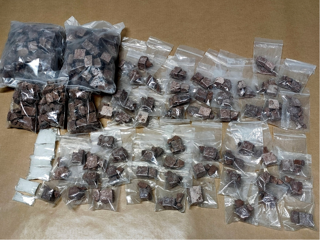 Several plastic bags containing brown cubes and white powder arranged on a tan surface.