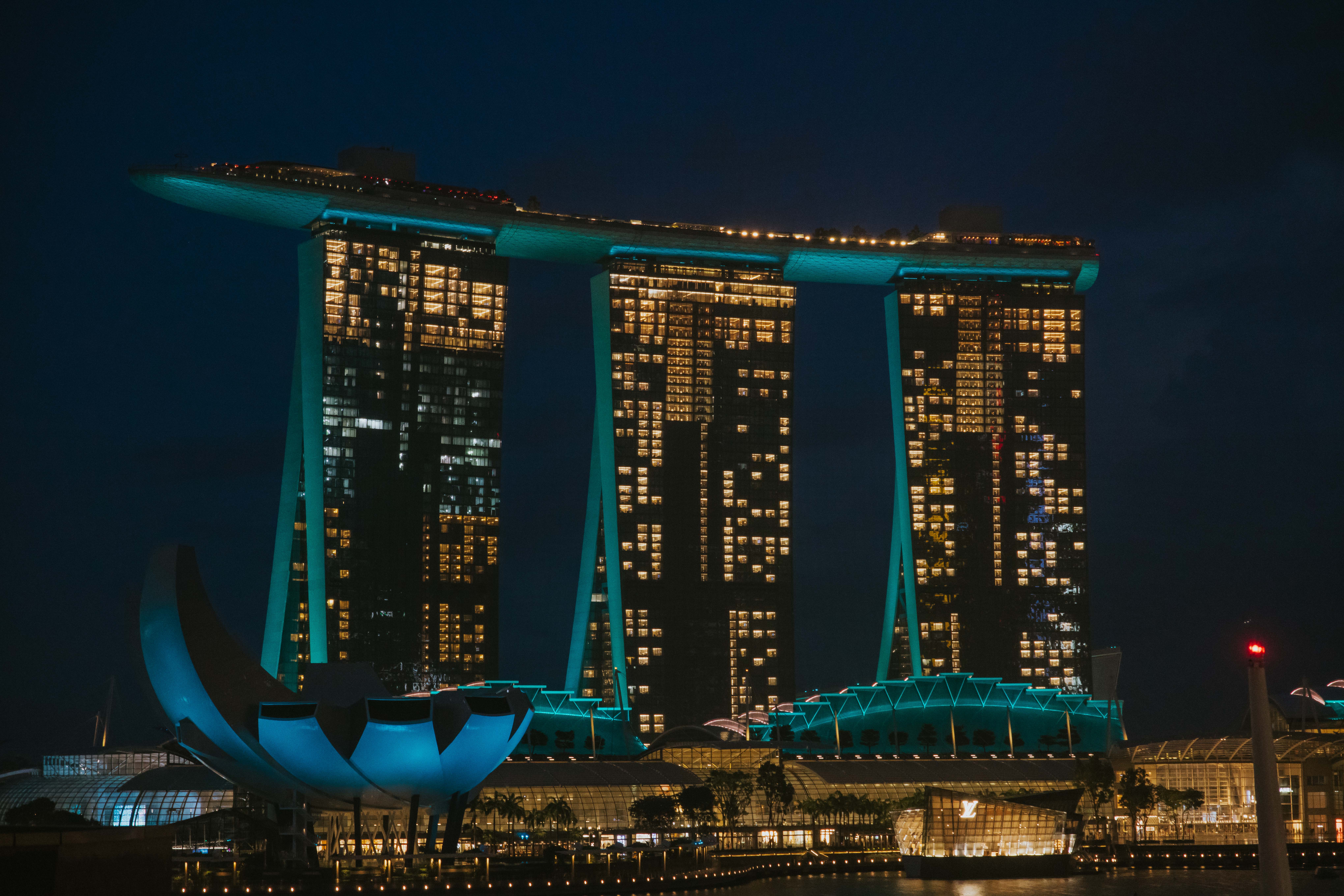Marina Bay Sands, Singapore at night. Three towers connected with a sky deck over a blue lotus shaped building.