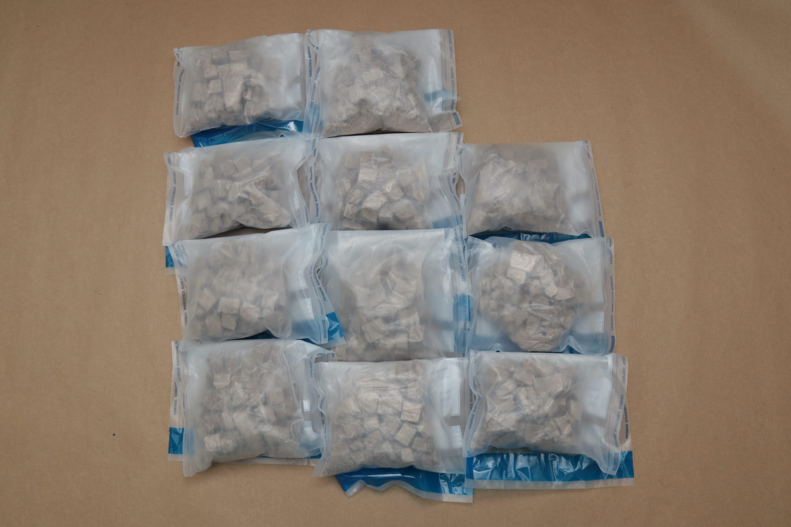 Eleven clear bags of tan, cube-shaped material, labeled "Central Narcotics Bureau".