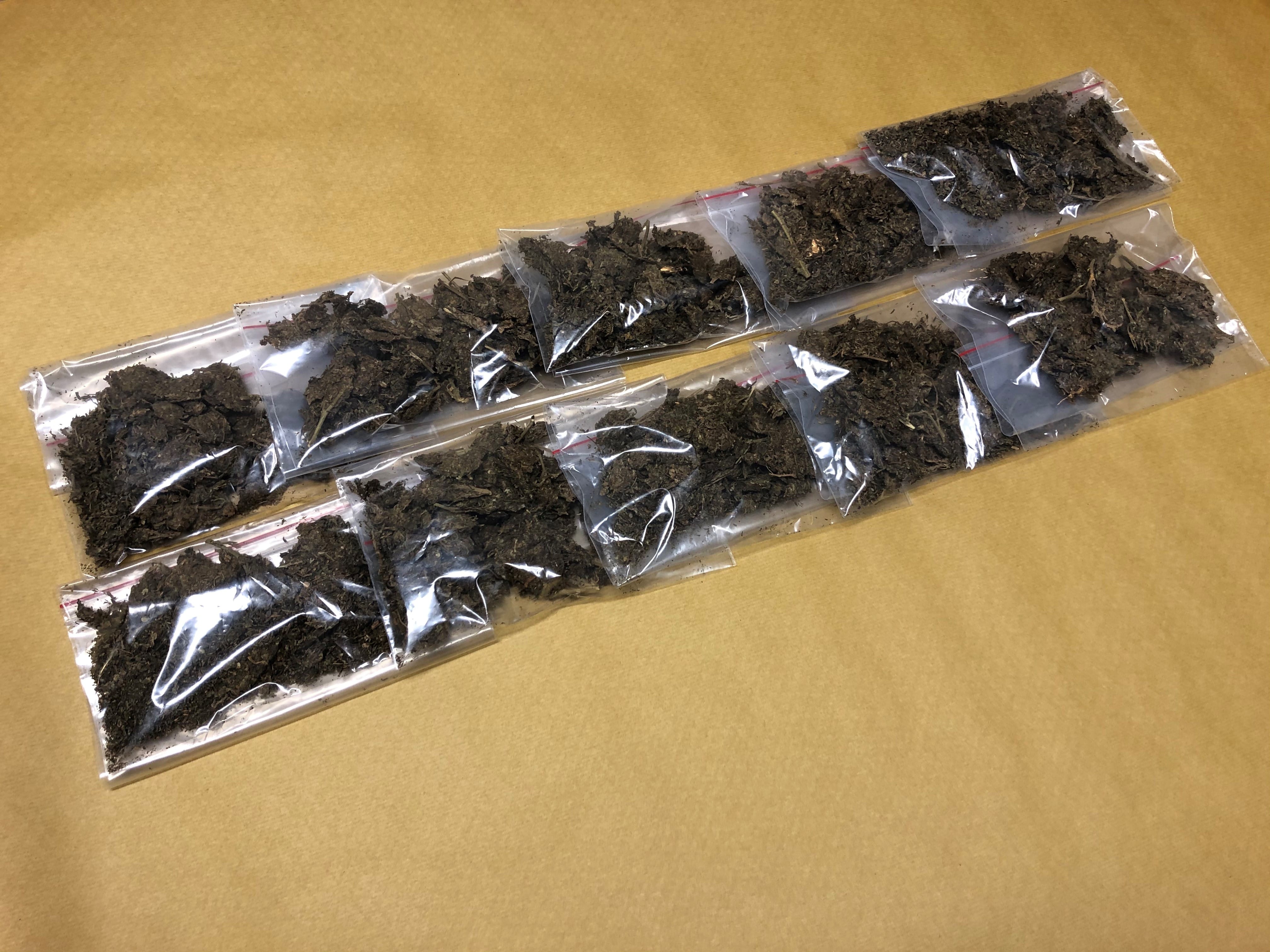 Nine small, clear plastic bags filled with dark brown organic material arranged on brown paper.