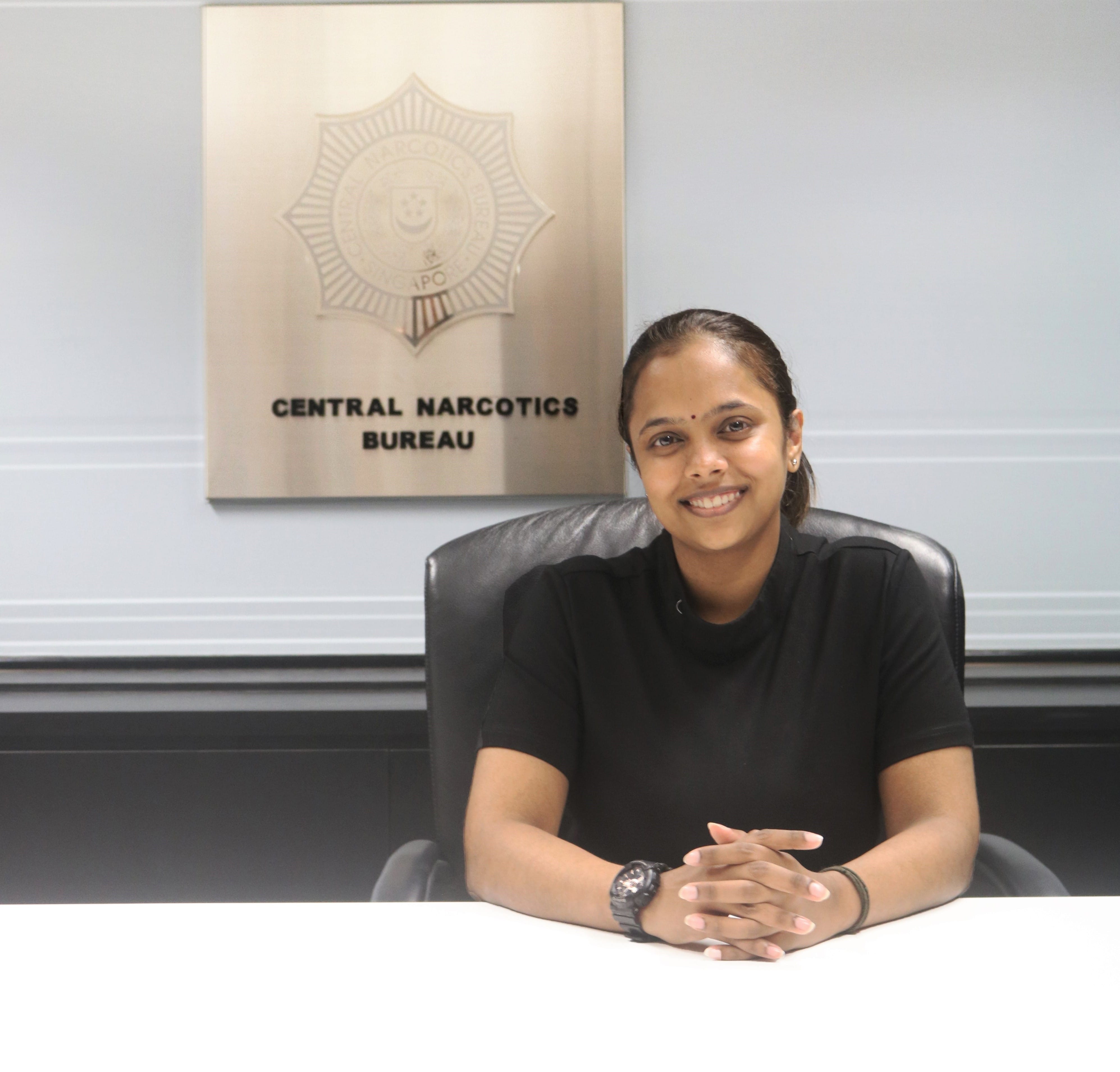 Subashiyni Ramakrishnan seated at the table with CNB signage behind her.