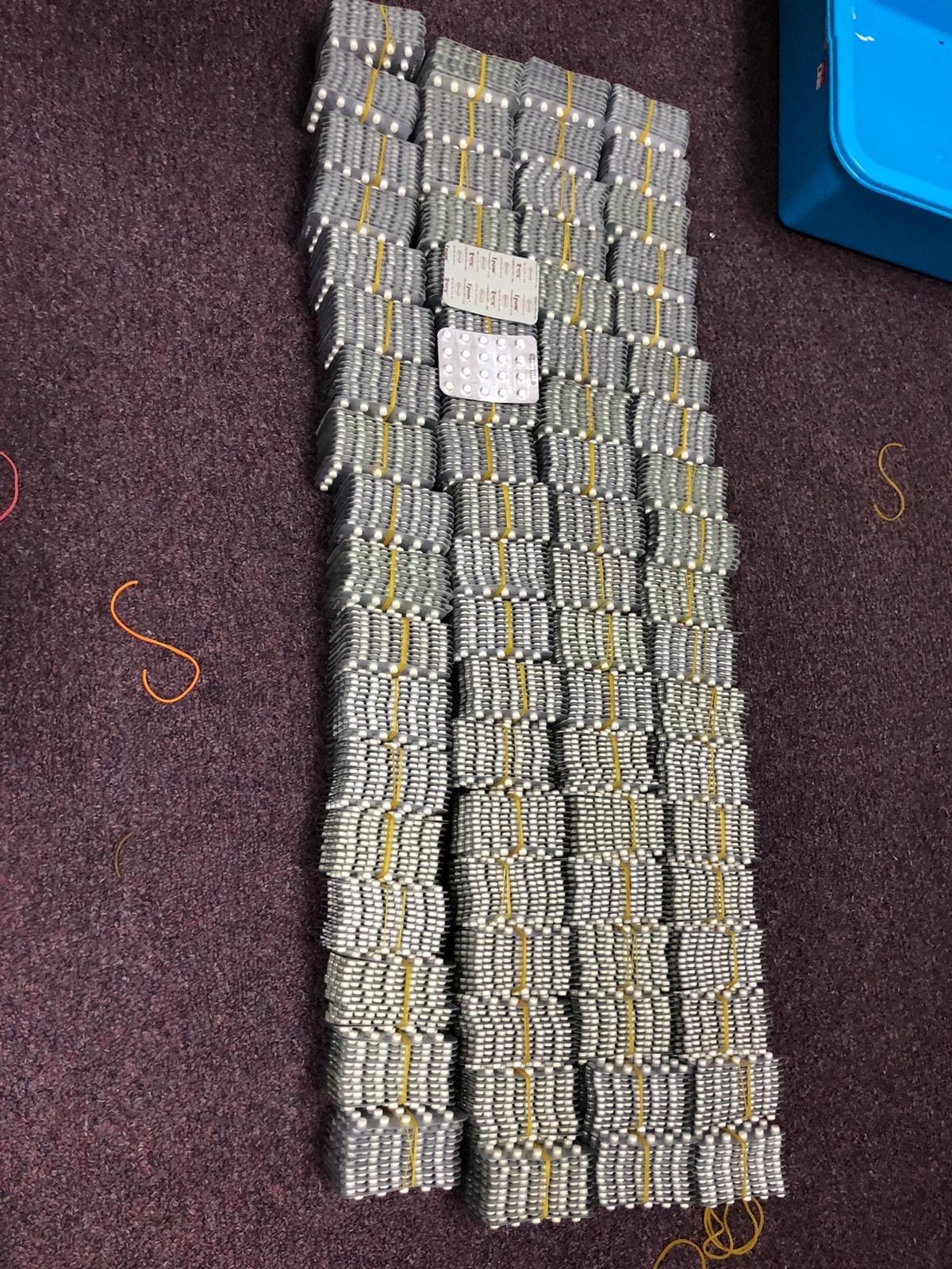 Stacks of pill packets bundled with rubber bands on a purple surface.