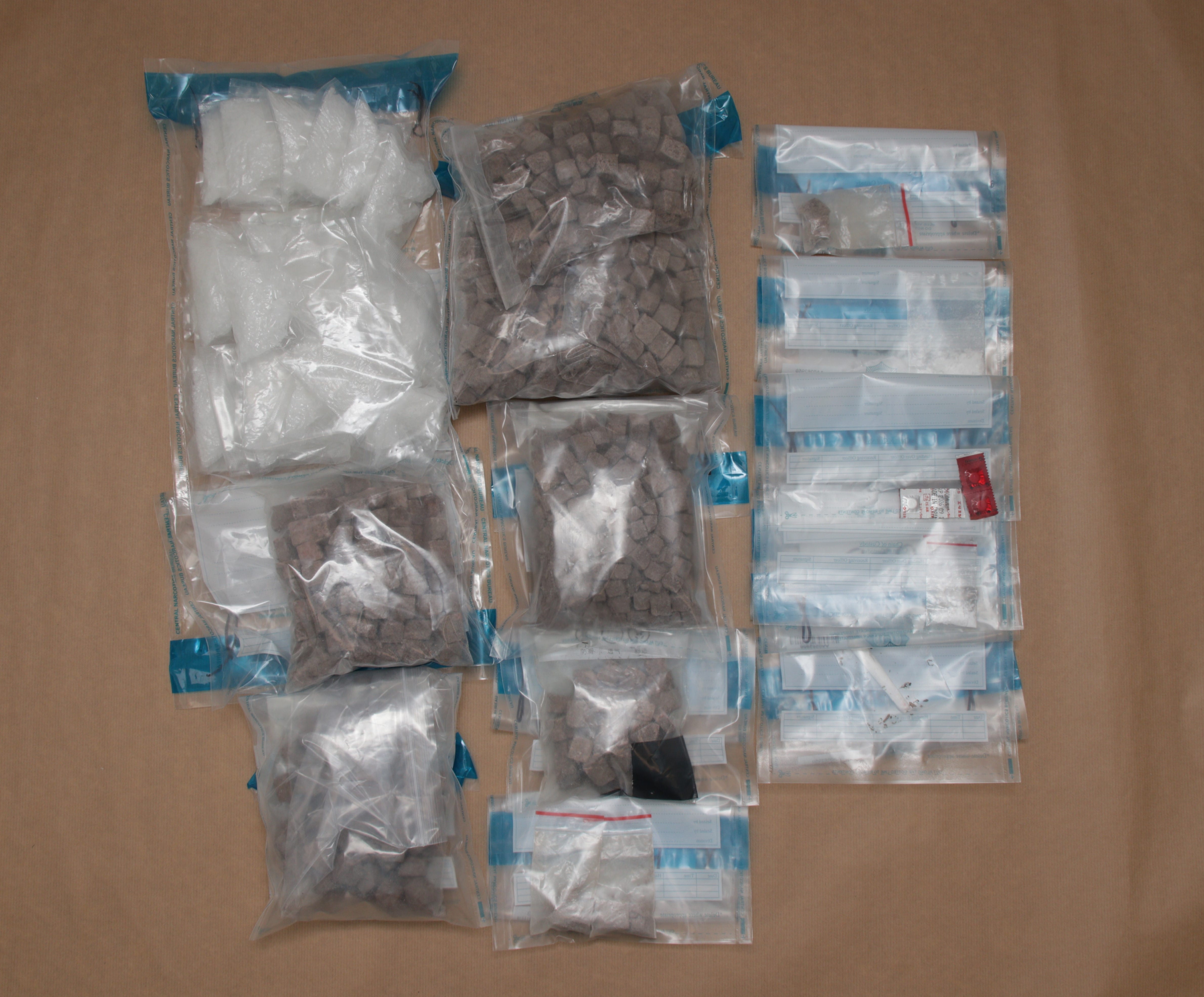 Sealed bags containing white crystals, brown cubes, loose powder, tablets, on a beige surface.