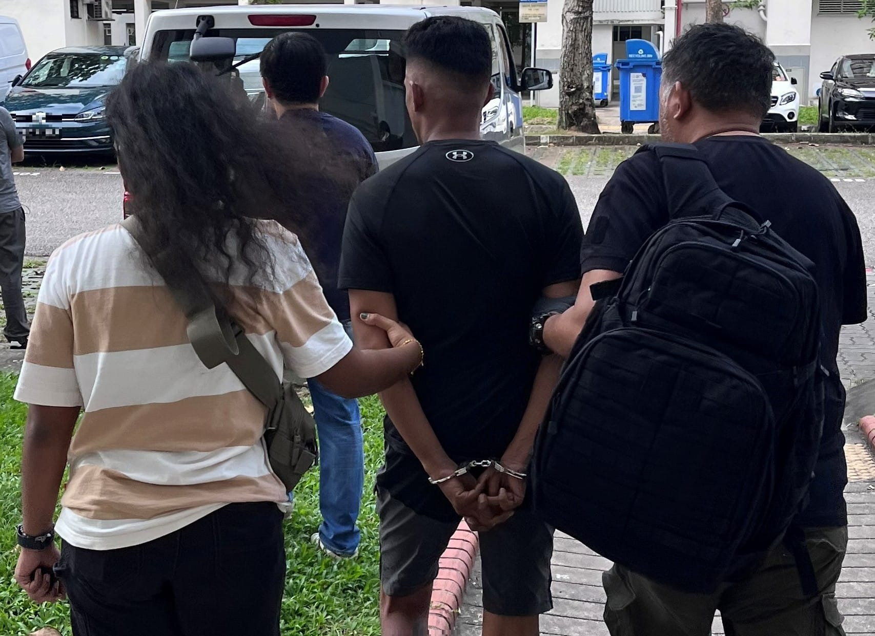 Person in Under Armour shirt being escorted with hands cuffed.