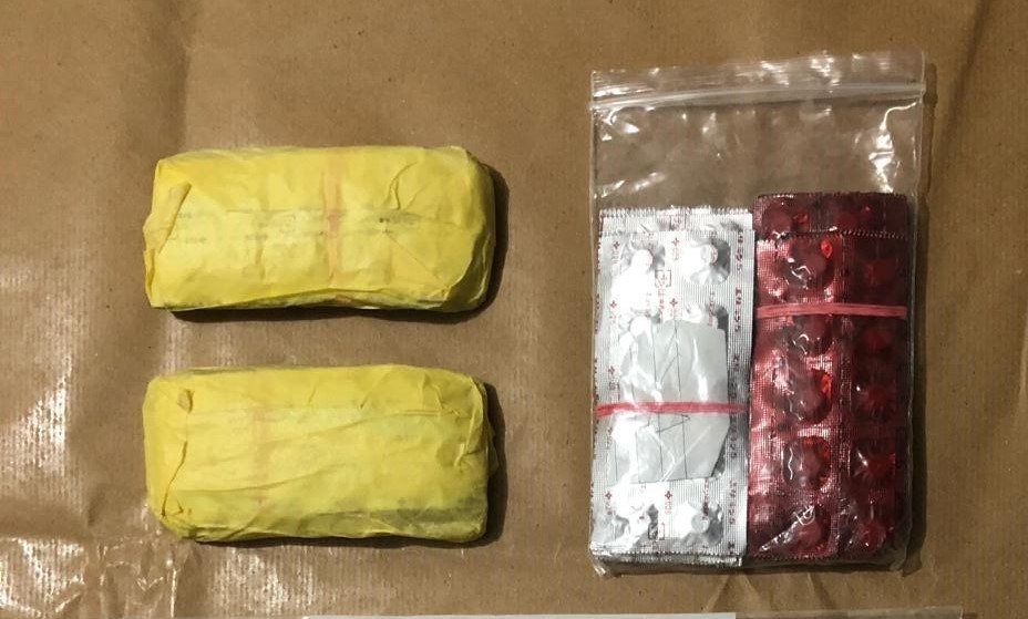Two yellow wrapped packets and a bag with red and white pill blister packs on brown paper.