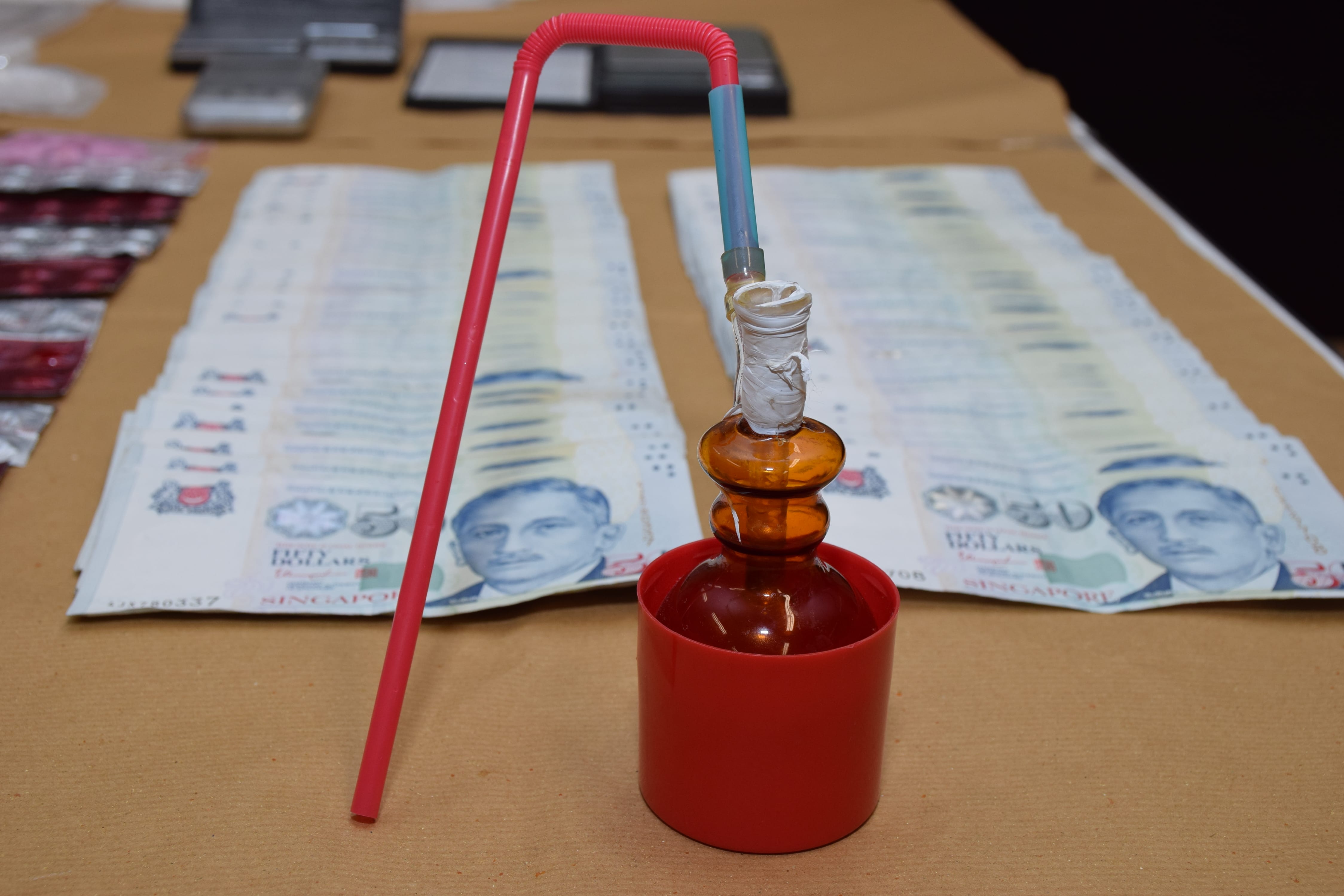 Table with cash, pills, scales and glass pipe with red straw and plastic container.