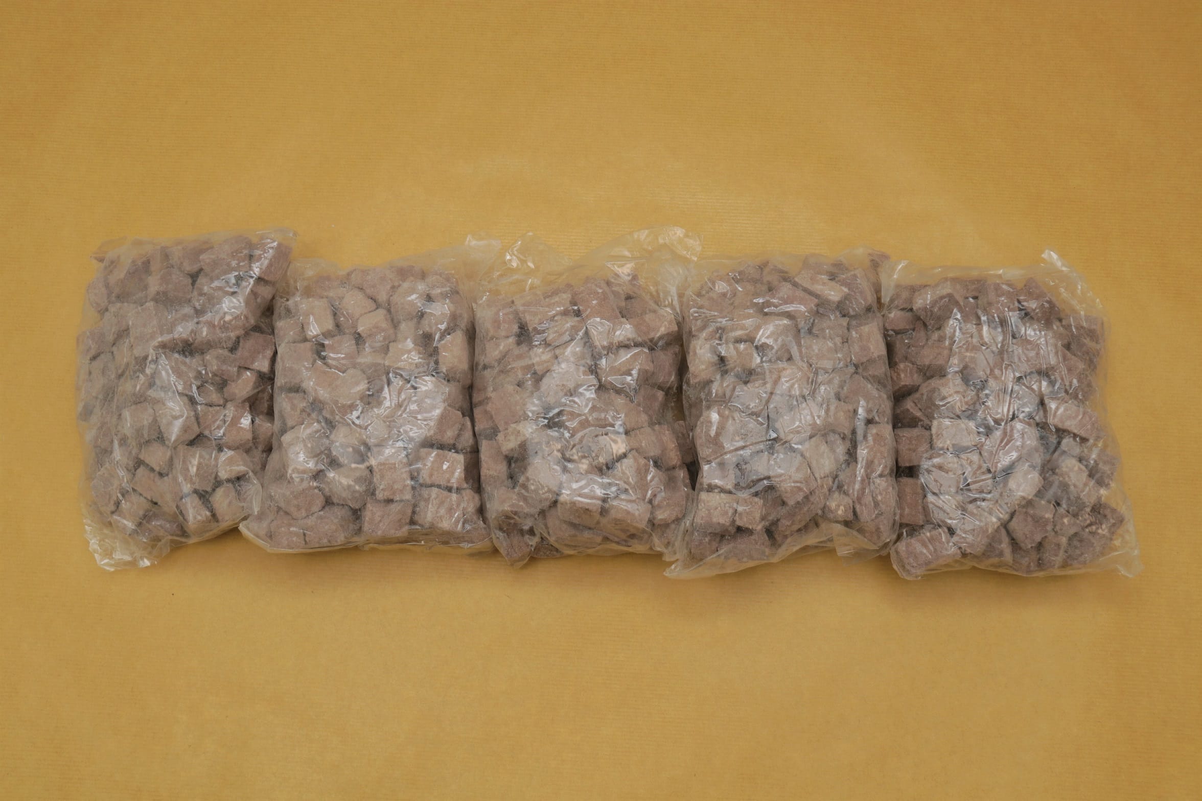 Five clear plastic bags filled with brown cube-shaped pieces on a yellow surface.