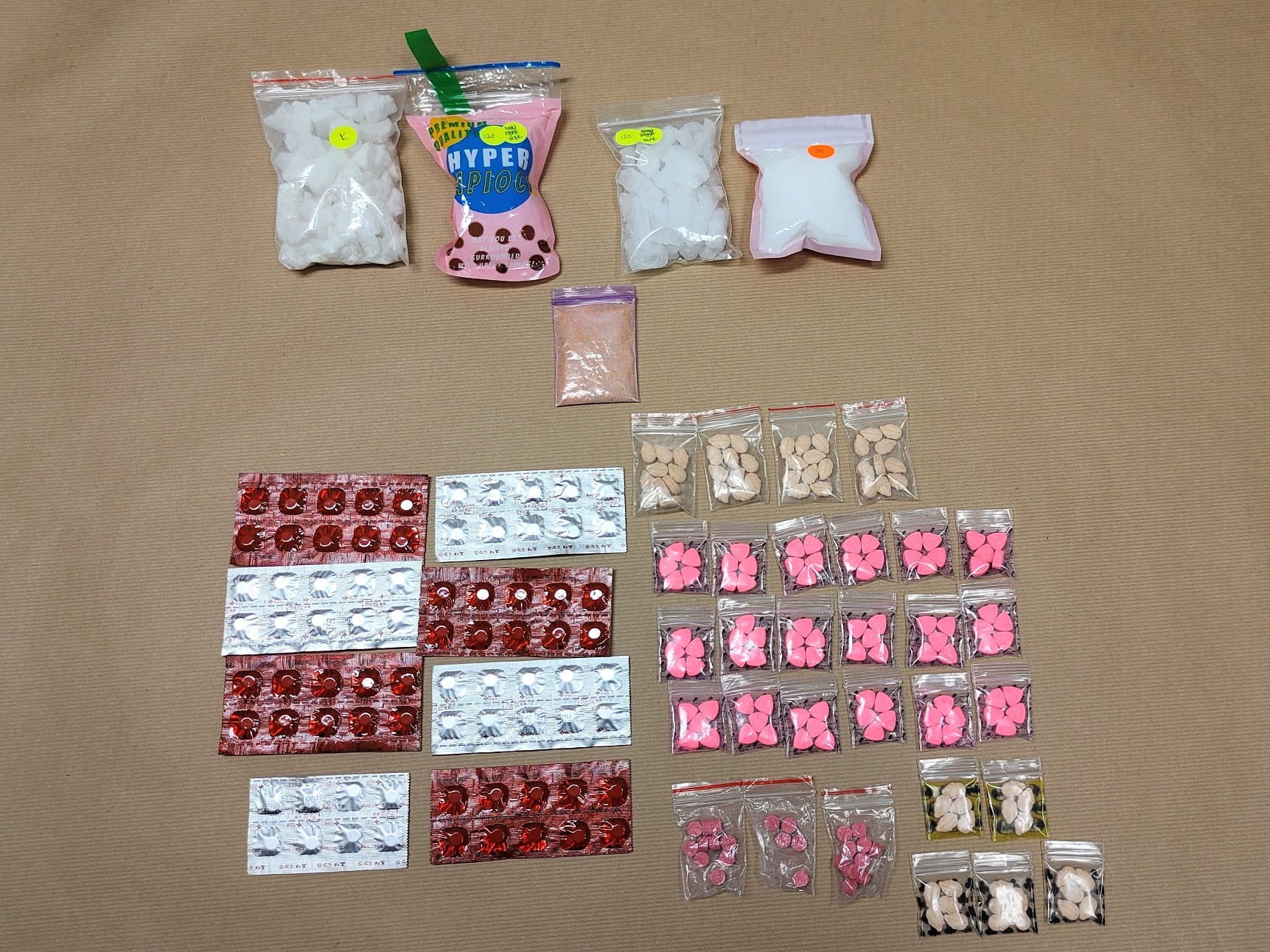 Assorted pills and powders in small bags and blister packs on a tan surface.