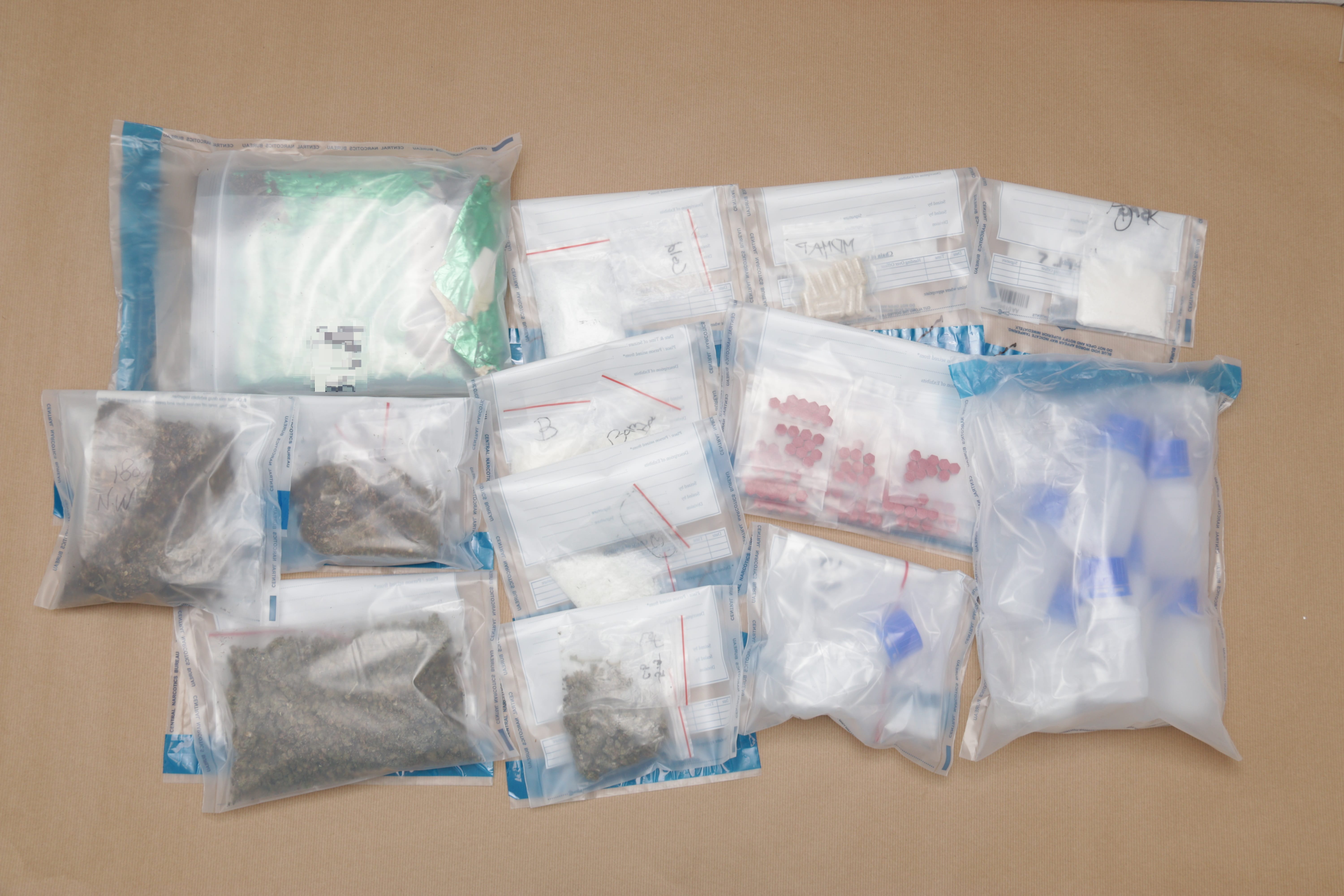 Multiple bags containing various materials, including powders, pills, bottles, and plant matter, displayed on a brown surface.