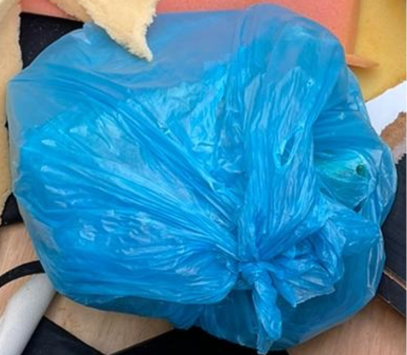 Knotted blue plastic bag full of discarded foam scraps and trim.