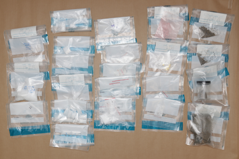 Rows of evidence bags with substances: white powder, pills, pink powder, dark herbs.