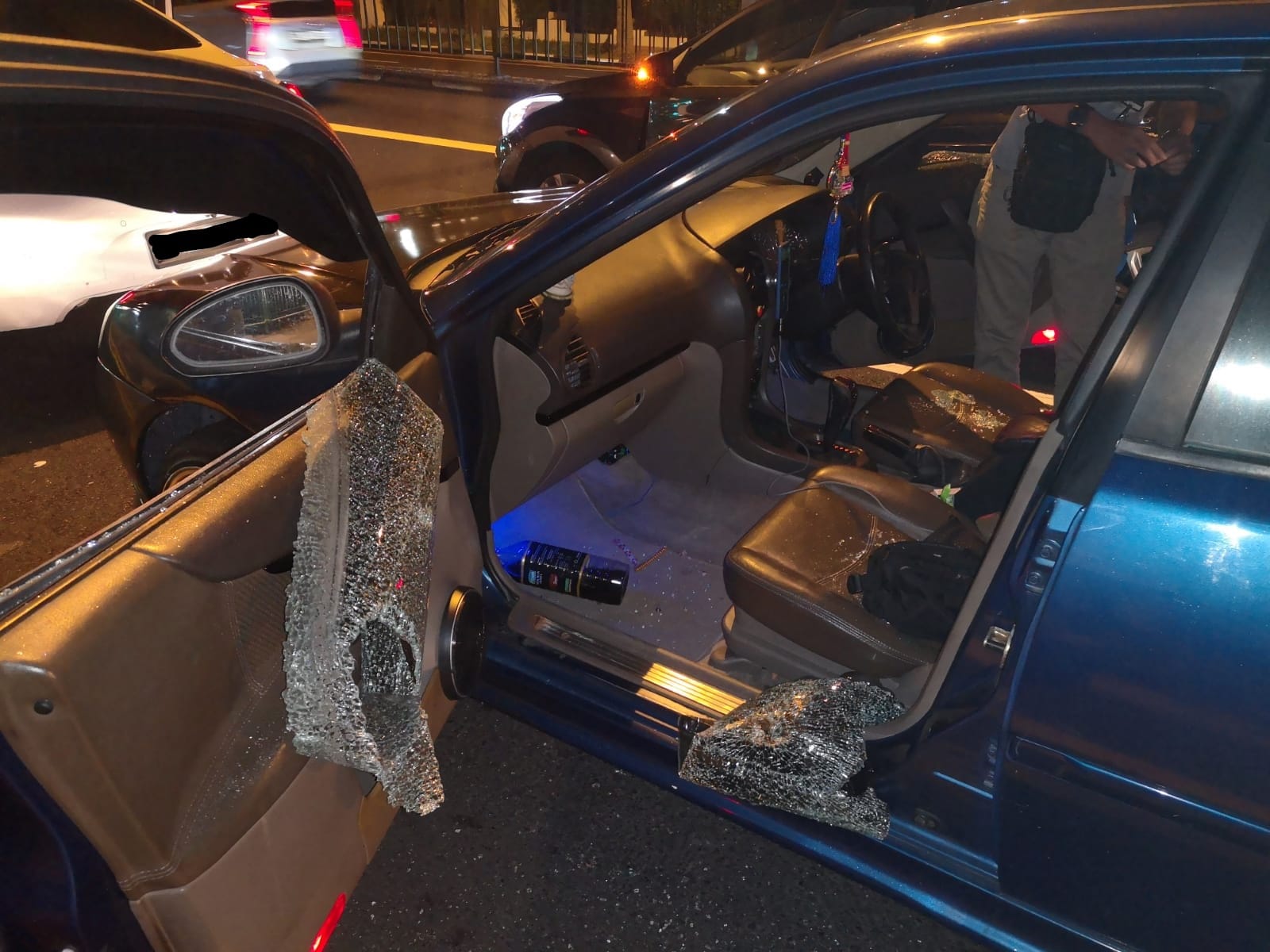 Blue car with shattered window, open door, damaged hood, and other vehicles visible.