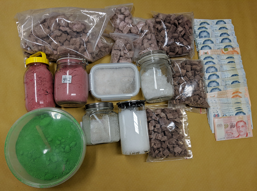 Containers of colored powders, bags of brown cubes, and stacks of Singaporean currency.