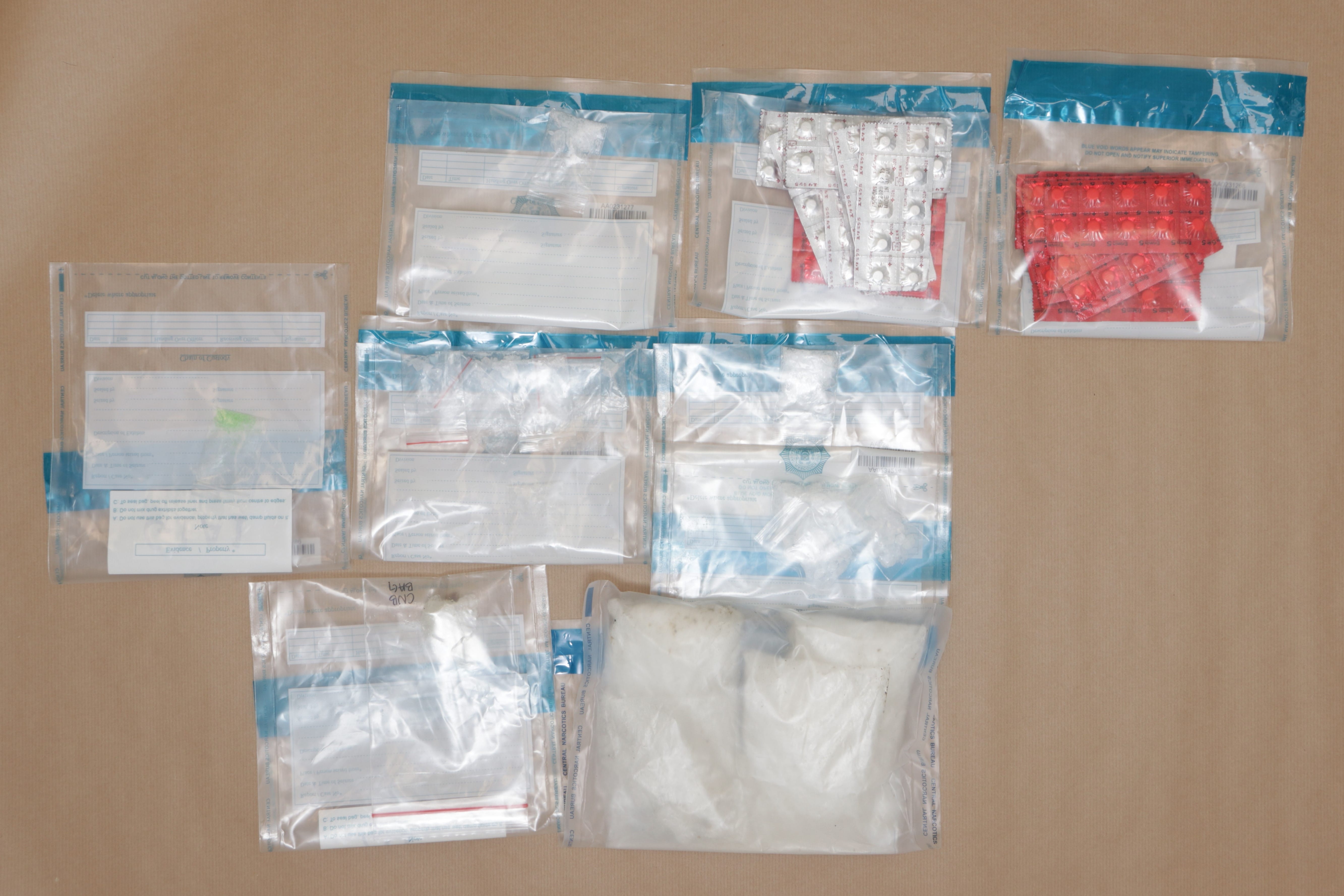 Evidence bags with pills and powder, on brown surface, labeled "Central Narcotics Bureau".