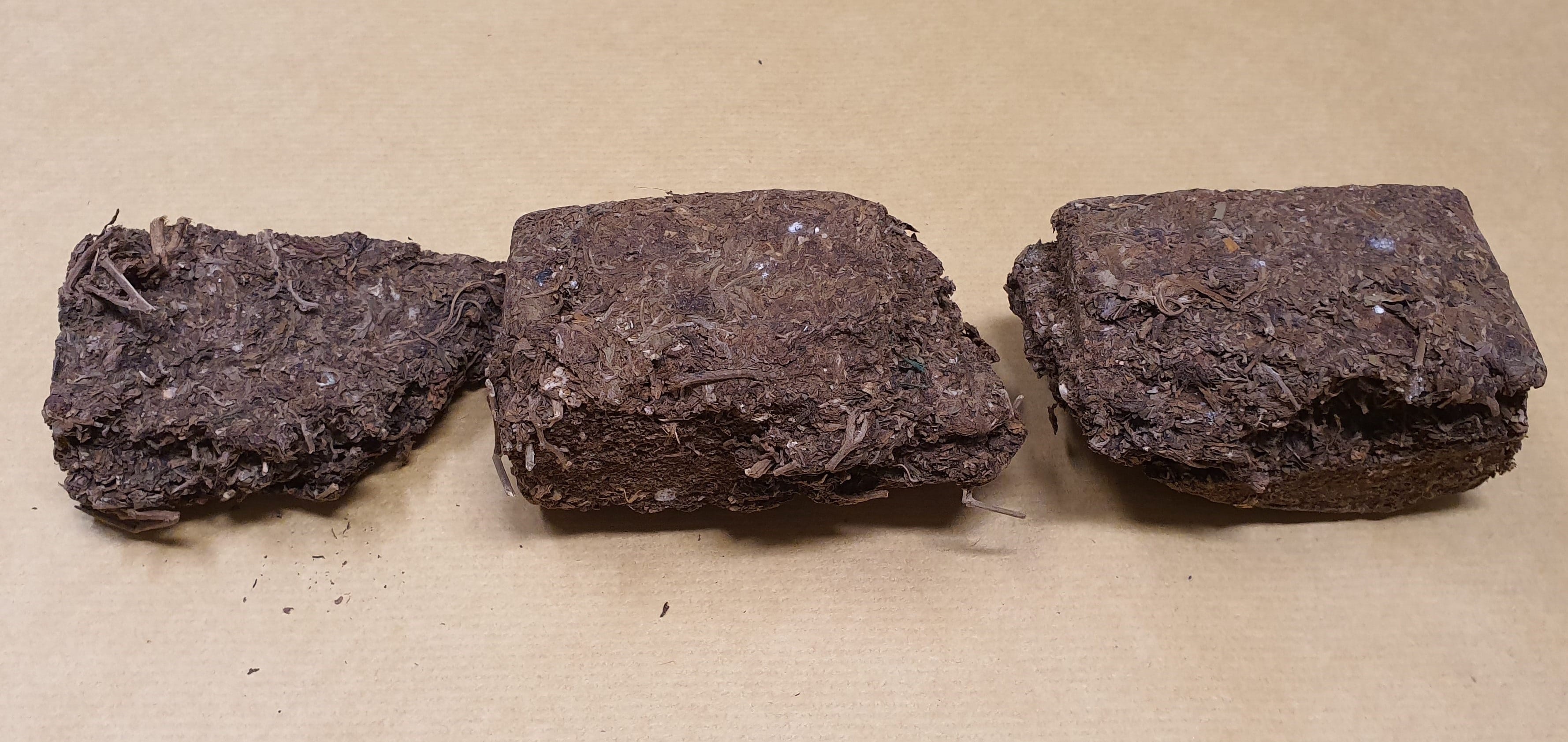 Three rectangular blocks of packed, dark brown plant material, possibly coir.